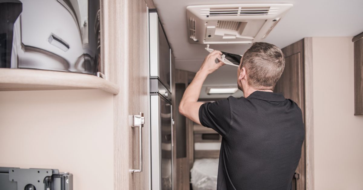 A man is fixing a ceiling fan in a camper van.