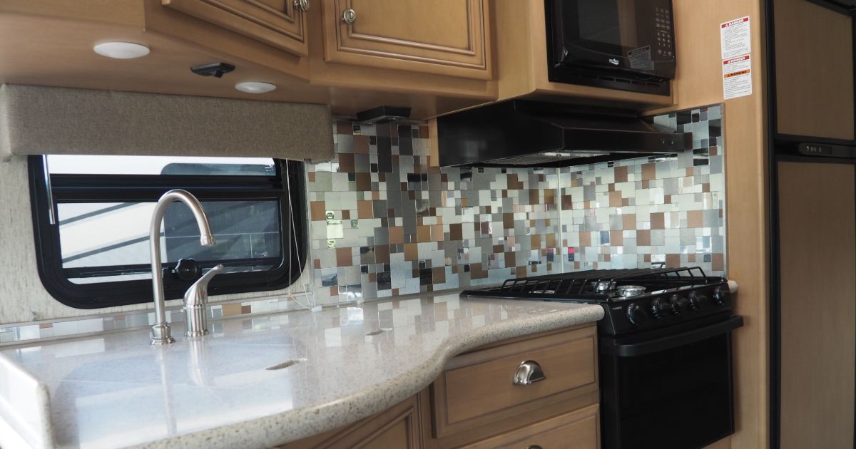 A kitchen in a rv with a sink , stove and microwave.