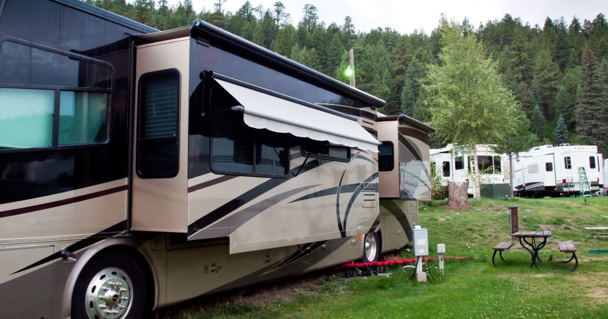 A large rv is parked in a grassy area next to a picnic table.