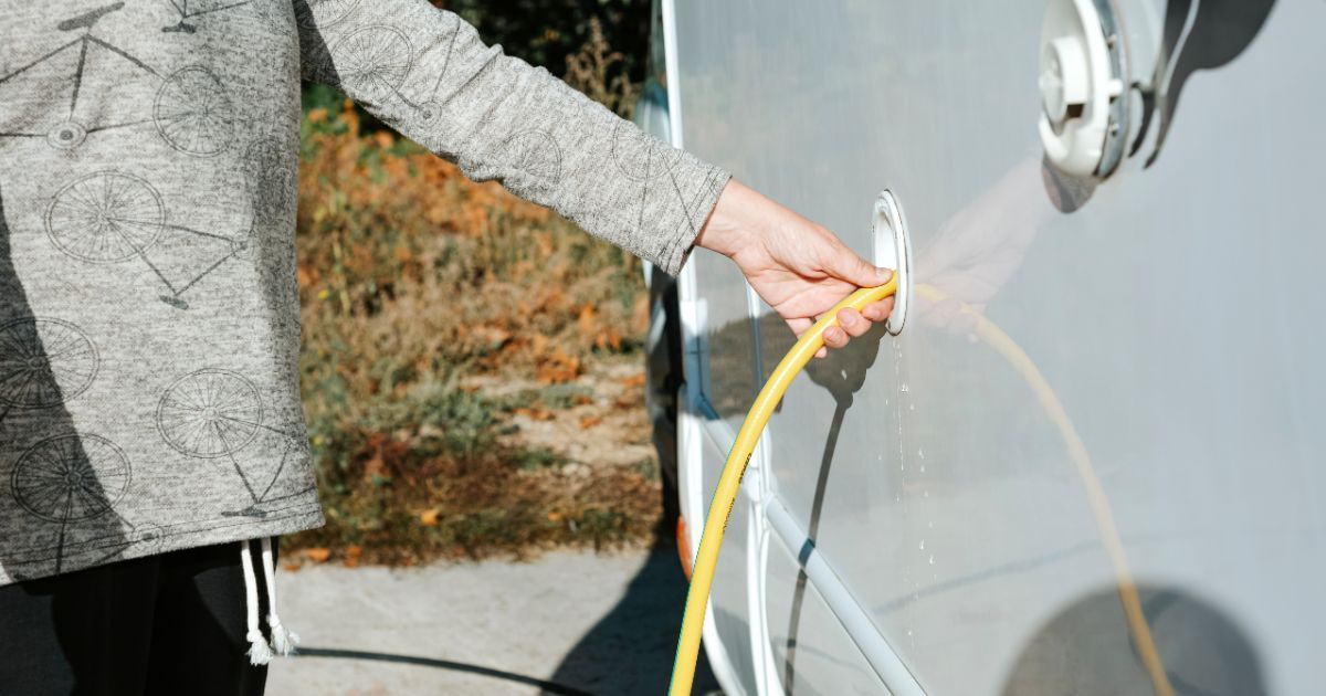 A person is plugging a hose into a camper.