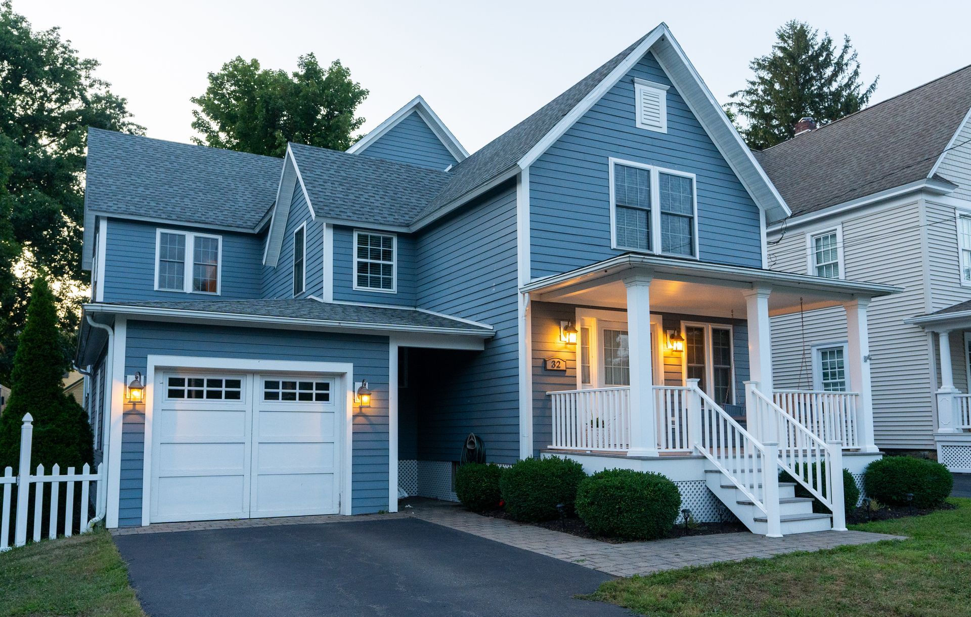 Blue house with white trim, garage, front porch, and small picket fence.