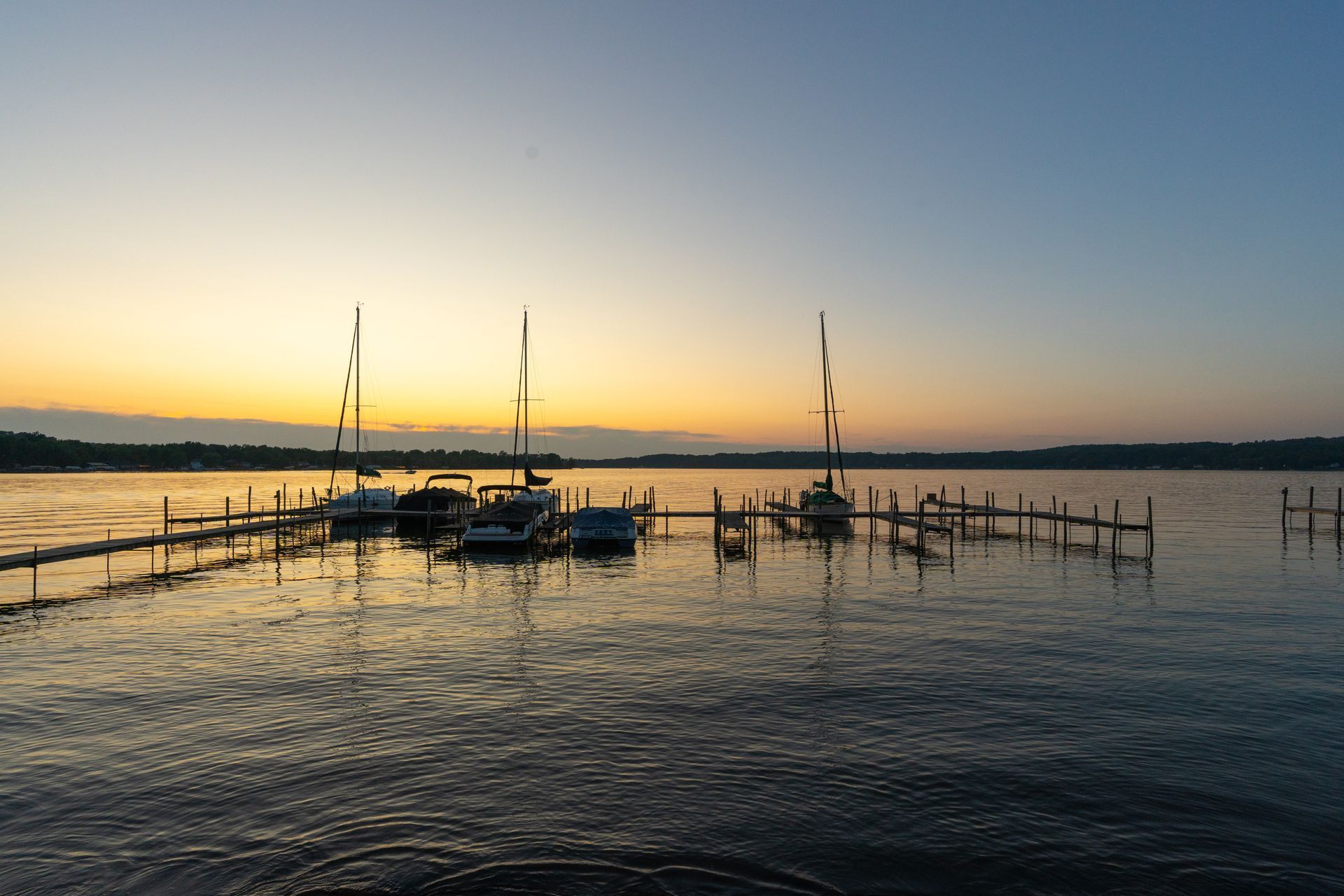 Boats docked at a pier on a lake at sunset; orange and blue sky reflects in the water.