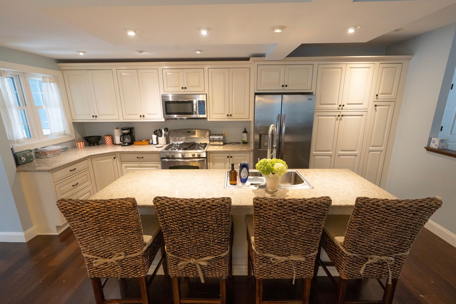 Kitchen with cream cabinets, island with four chairs, stainless steel appliances, and a window.