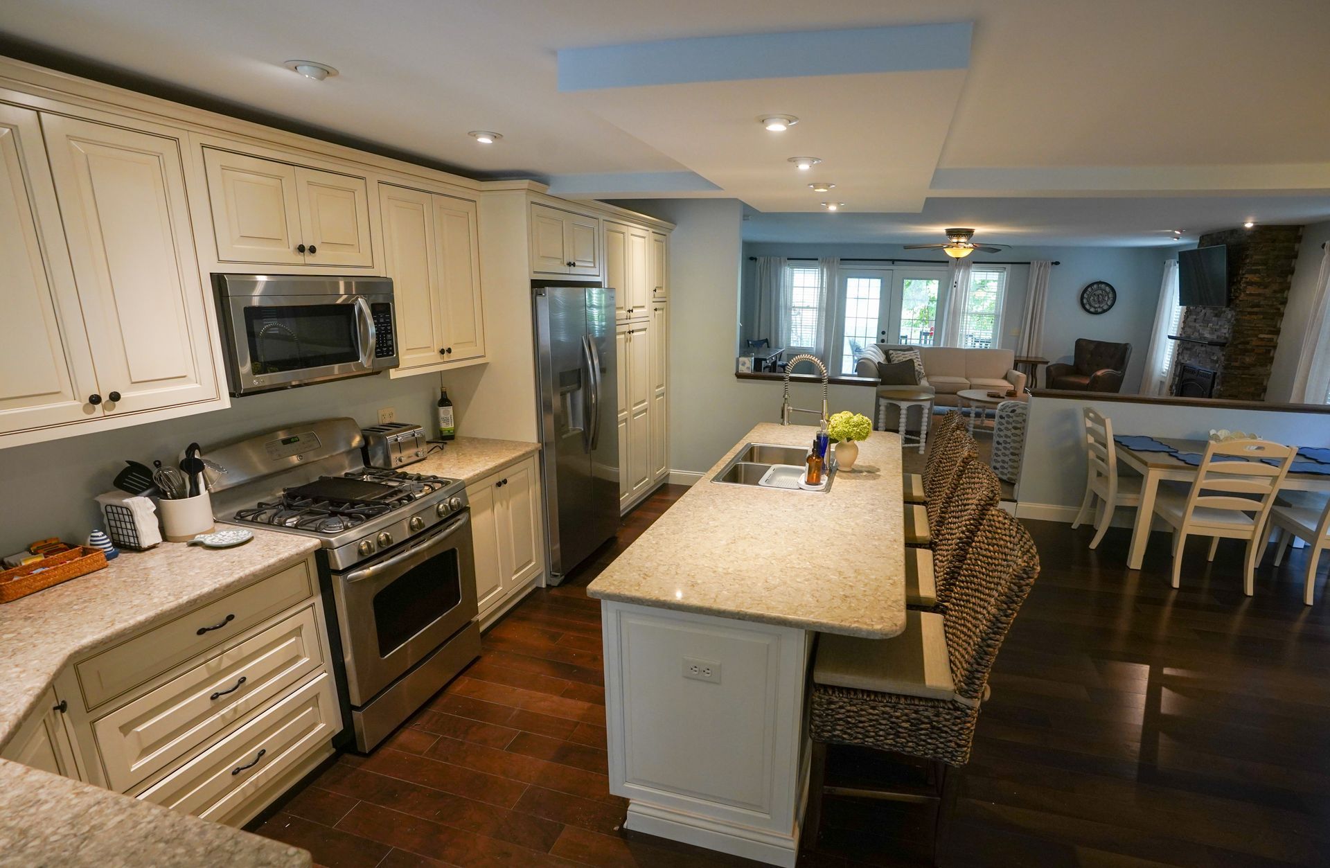 Kitchen with white cabinets, stainless steel appliances, island with seating, and dark wood floors.