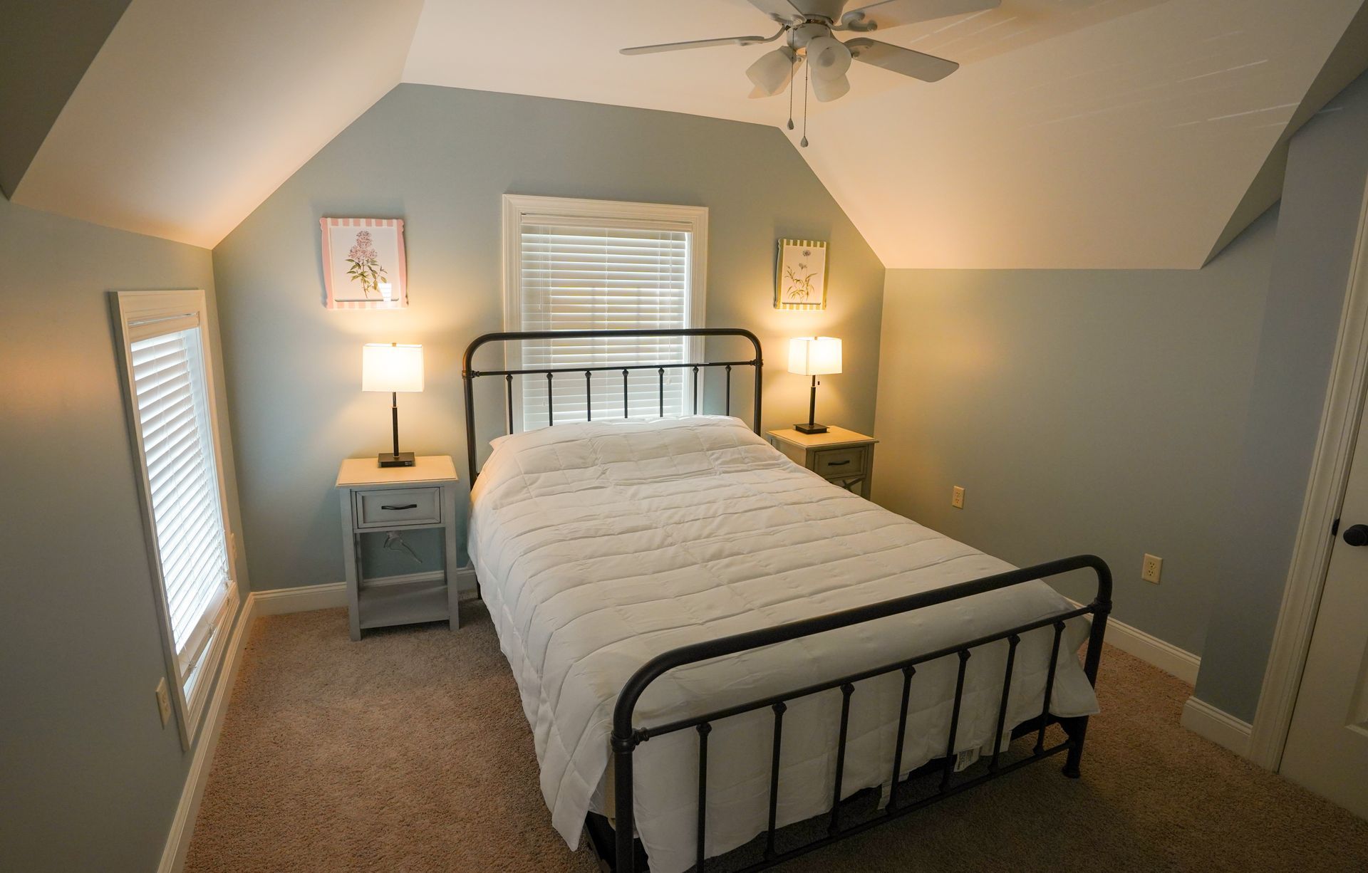 Bedroom with blue walls, metal bed, bedside tables with lamps, and carpet.