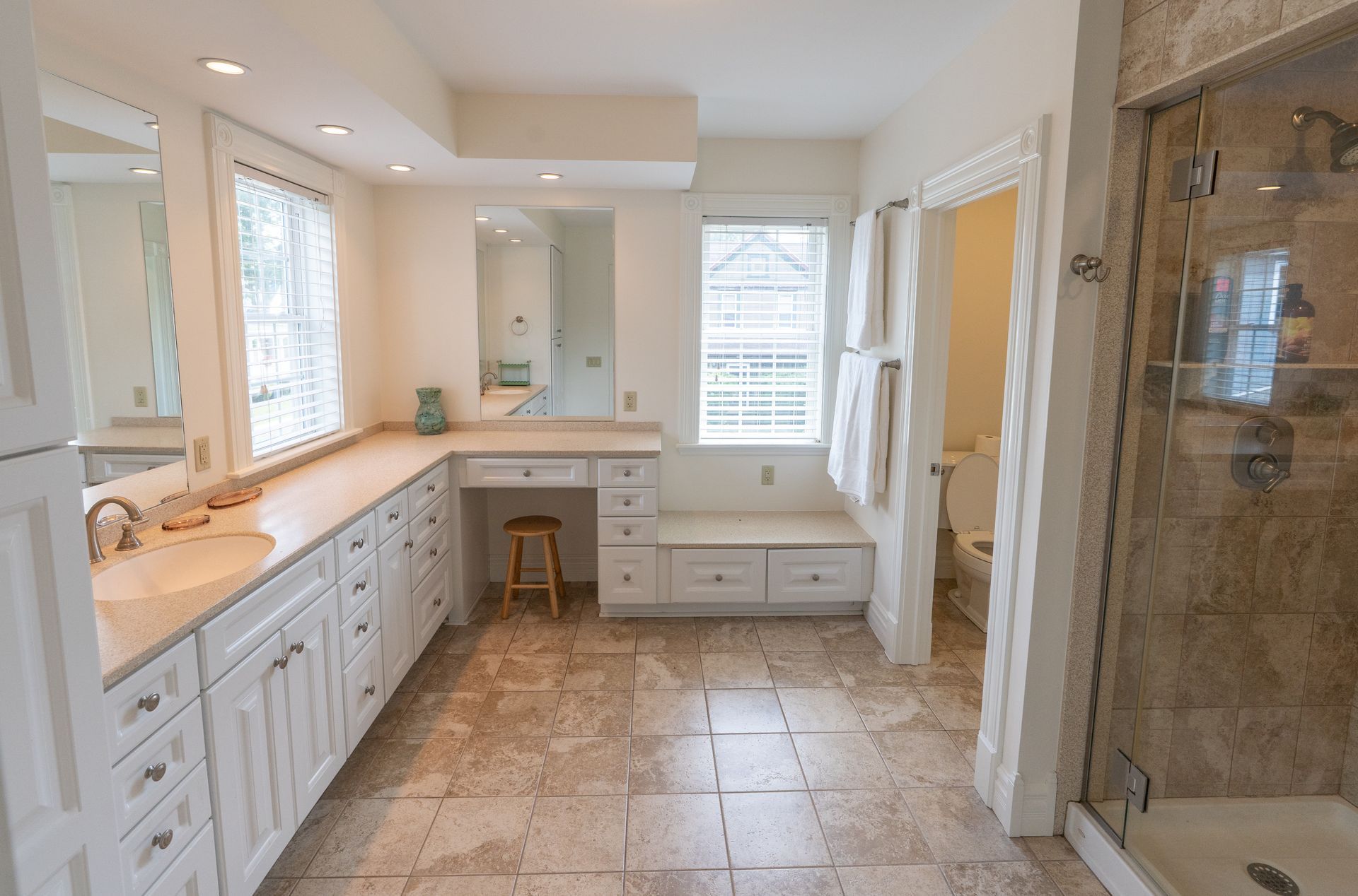 Spacious, bright bathroom with white cabinets, a vanity, and a large stone shower.