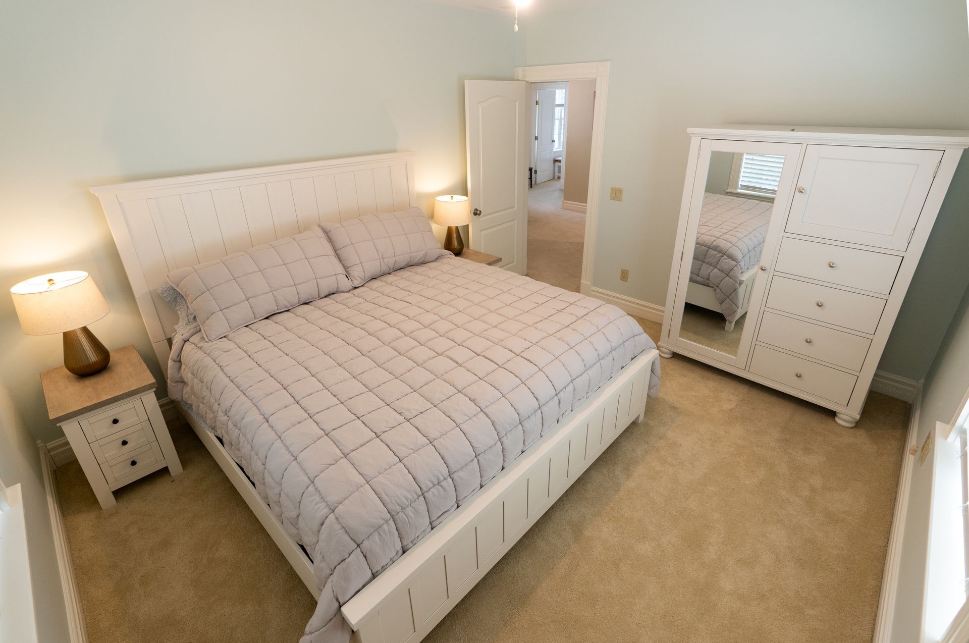 Bedroom with white bed, nightstand, and wardrobe; light blue walls, beige carpet.
