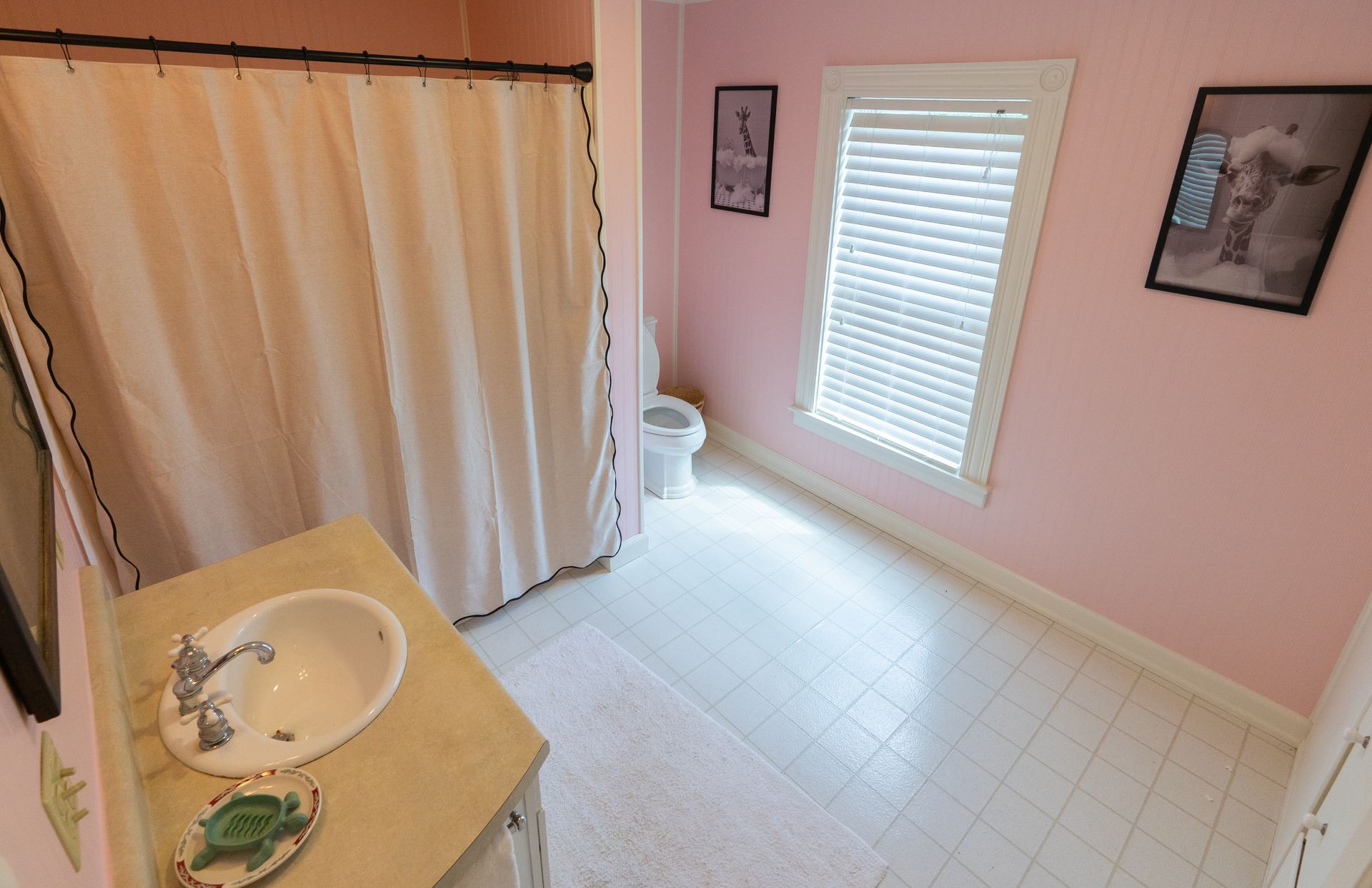 Pink bathroom with a shower, toilet, sink, and window with blinds.