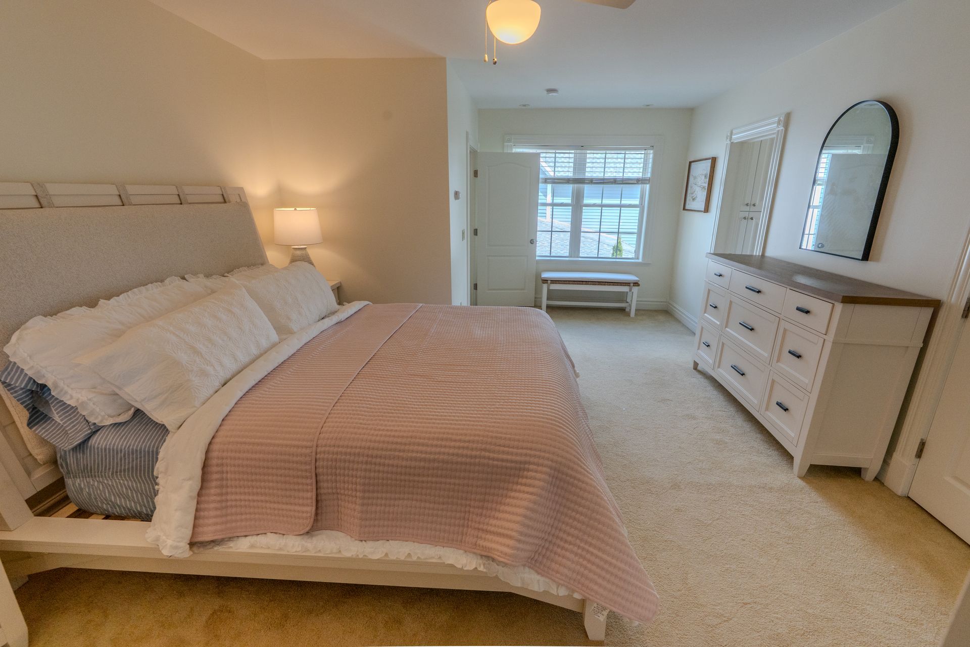 Bedroom with a bed, dresser, and doorway to a window seat. Pink and white bedding.