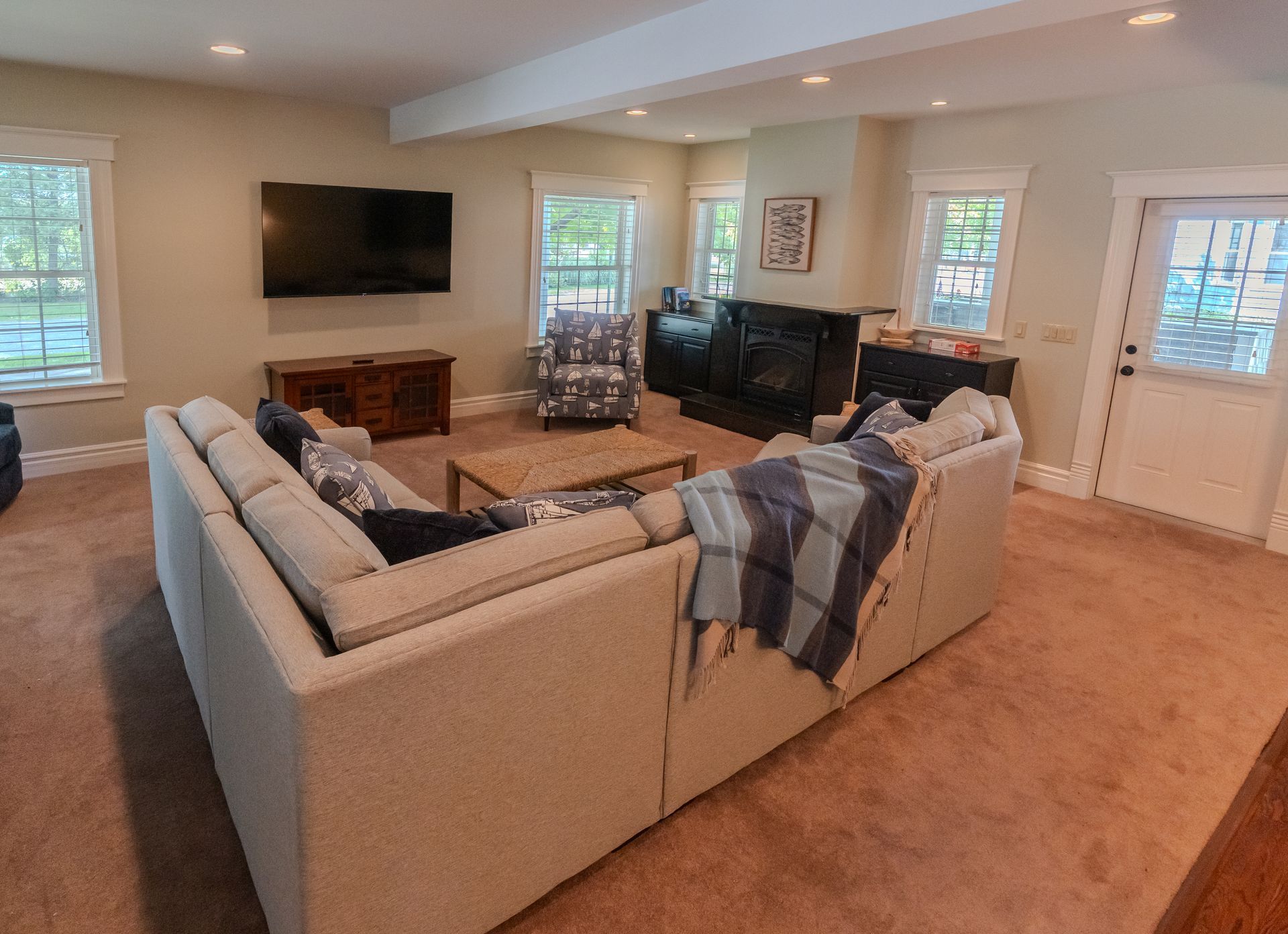 Spacious living room with sectional sofa, TV, fireplace, windows, and neutral carpet.