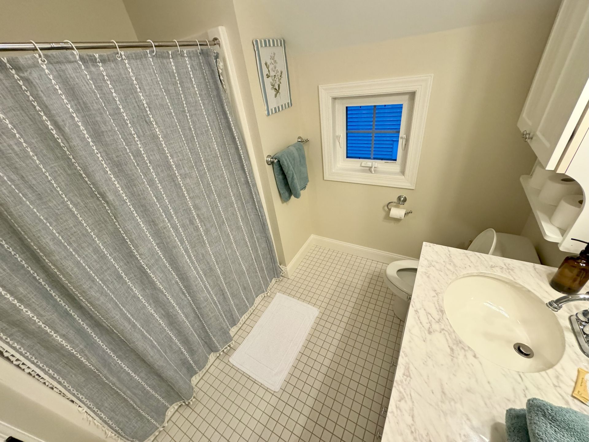 Bathroom with a gray shower curtain, white sink, toilet, and a small window.