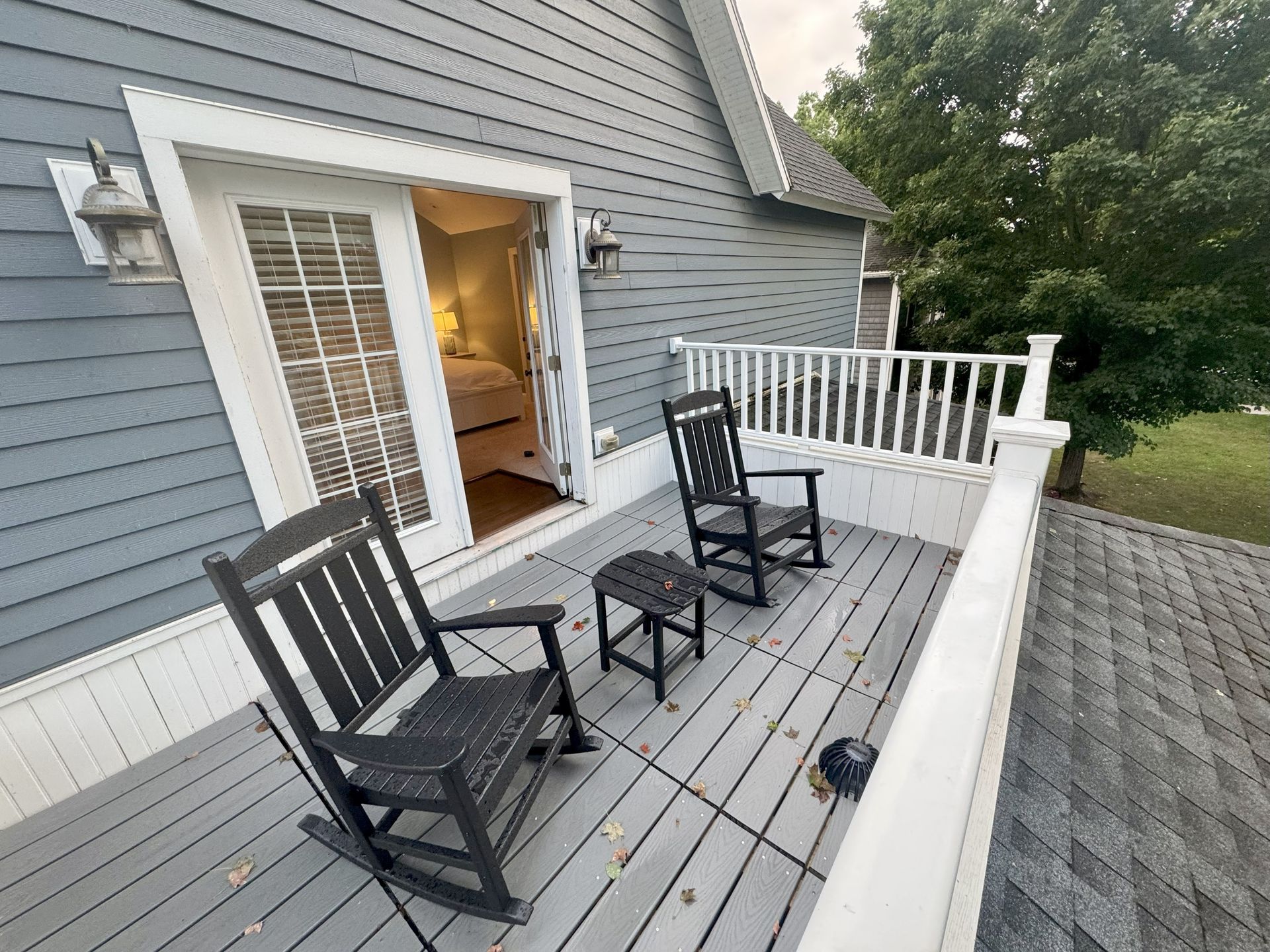 Two black rocking chairs on a gray deck overlooking a yard, with a doorway to a bedroom.