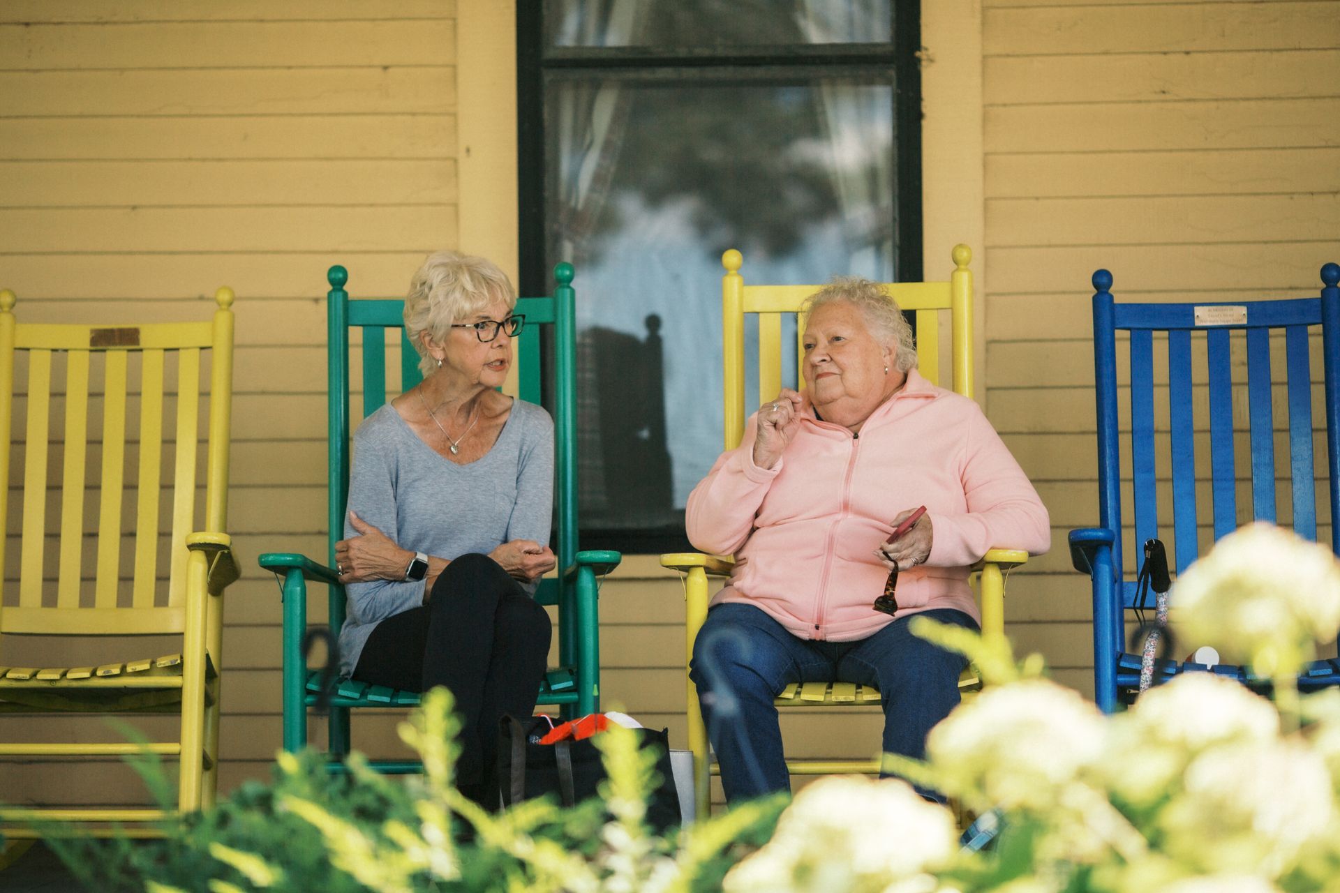 Covered porch with gray siding, rocking chairs, and a dark table set for a meal.