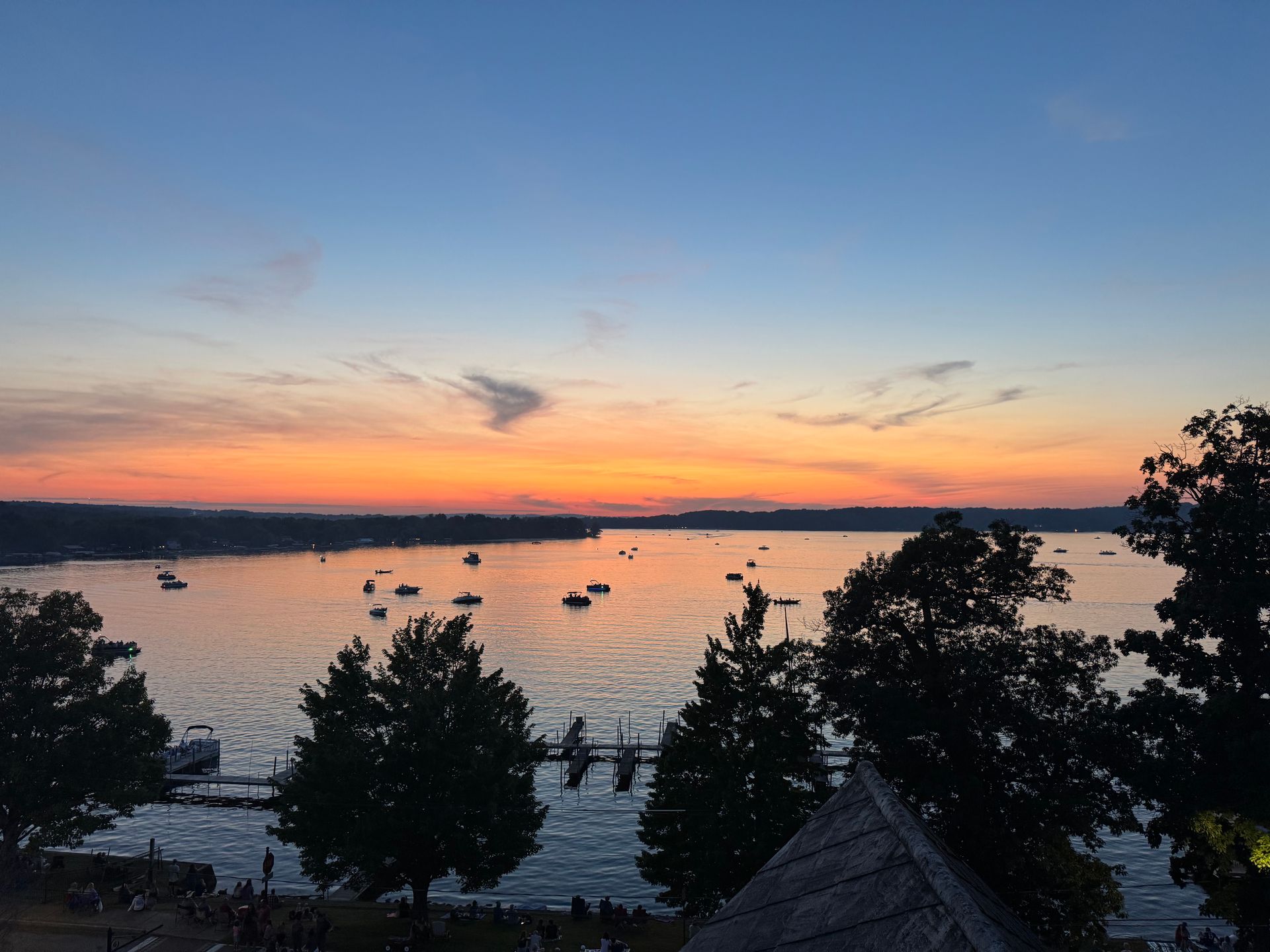 Sunset over a bay filled with boats; orange and blue sky; trees in foreground.