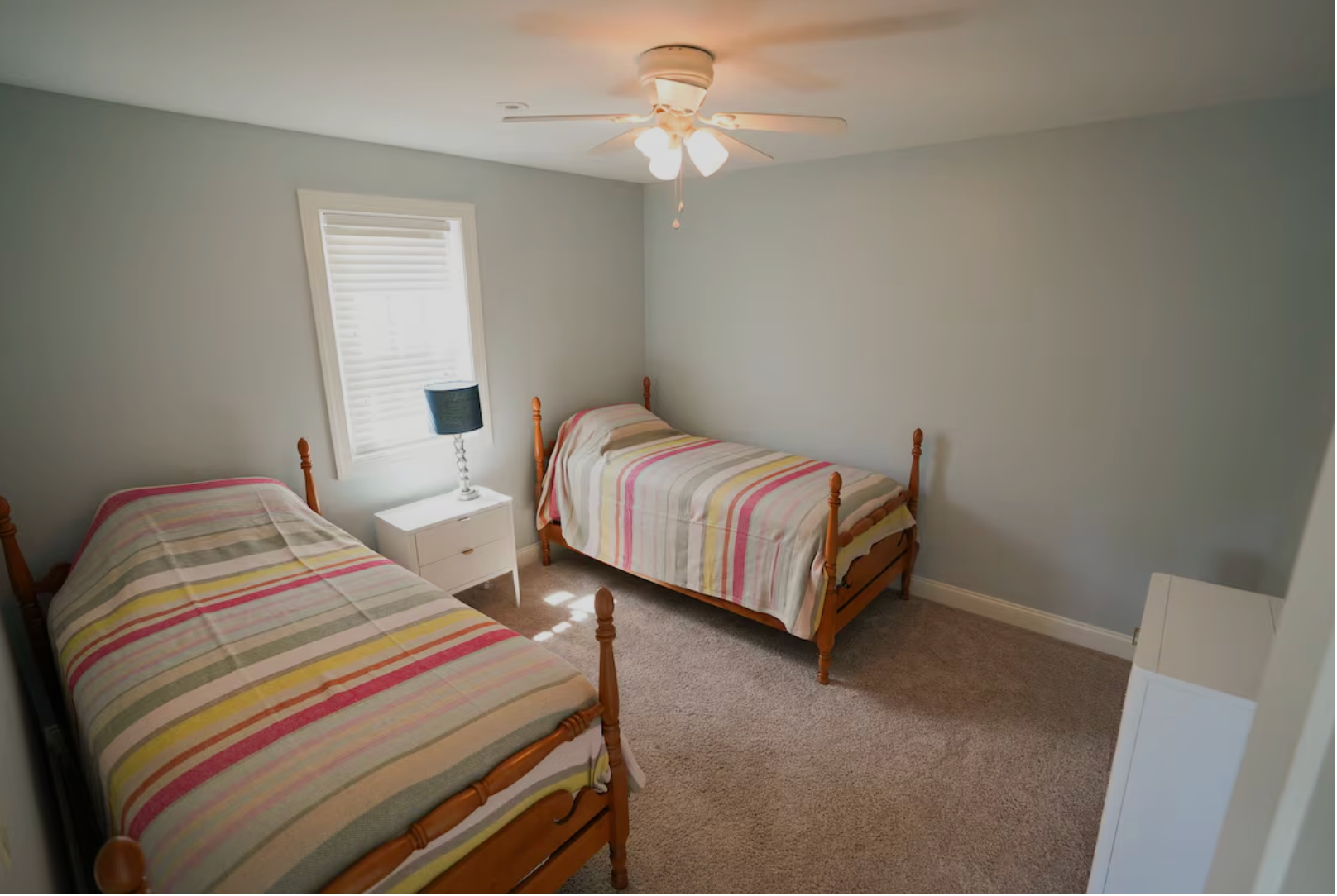 Two twin beds in a room with light blue walls, a window, and beige carpet.