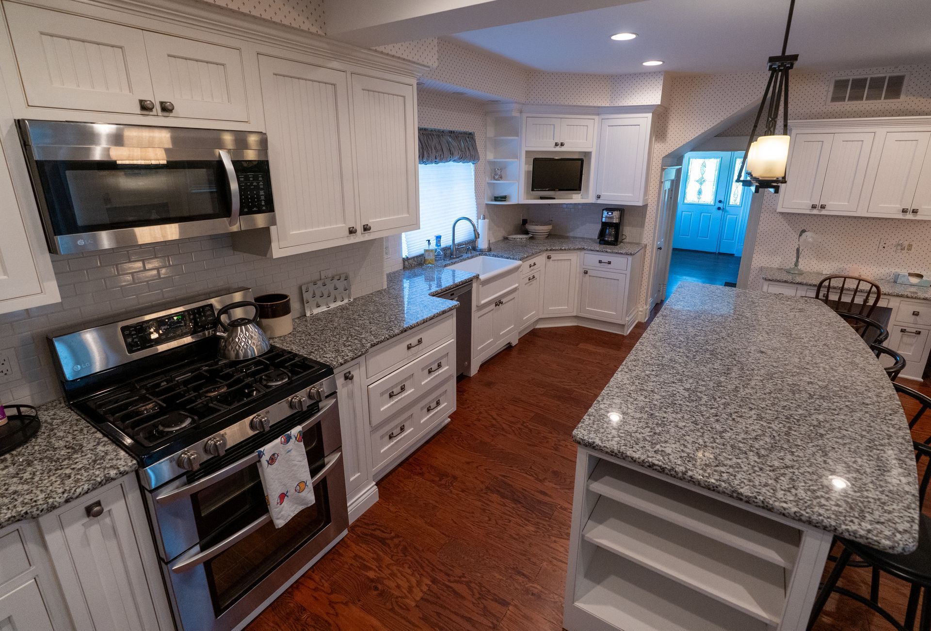 White kitchen with stainless steel appliances, granite countertops, and hardwood floors.