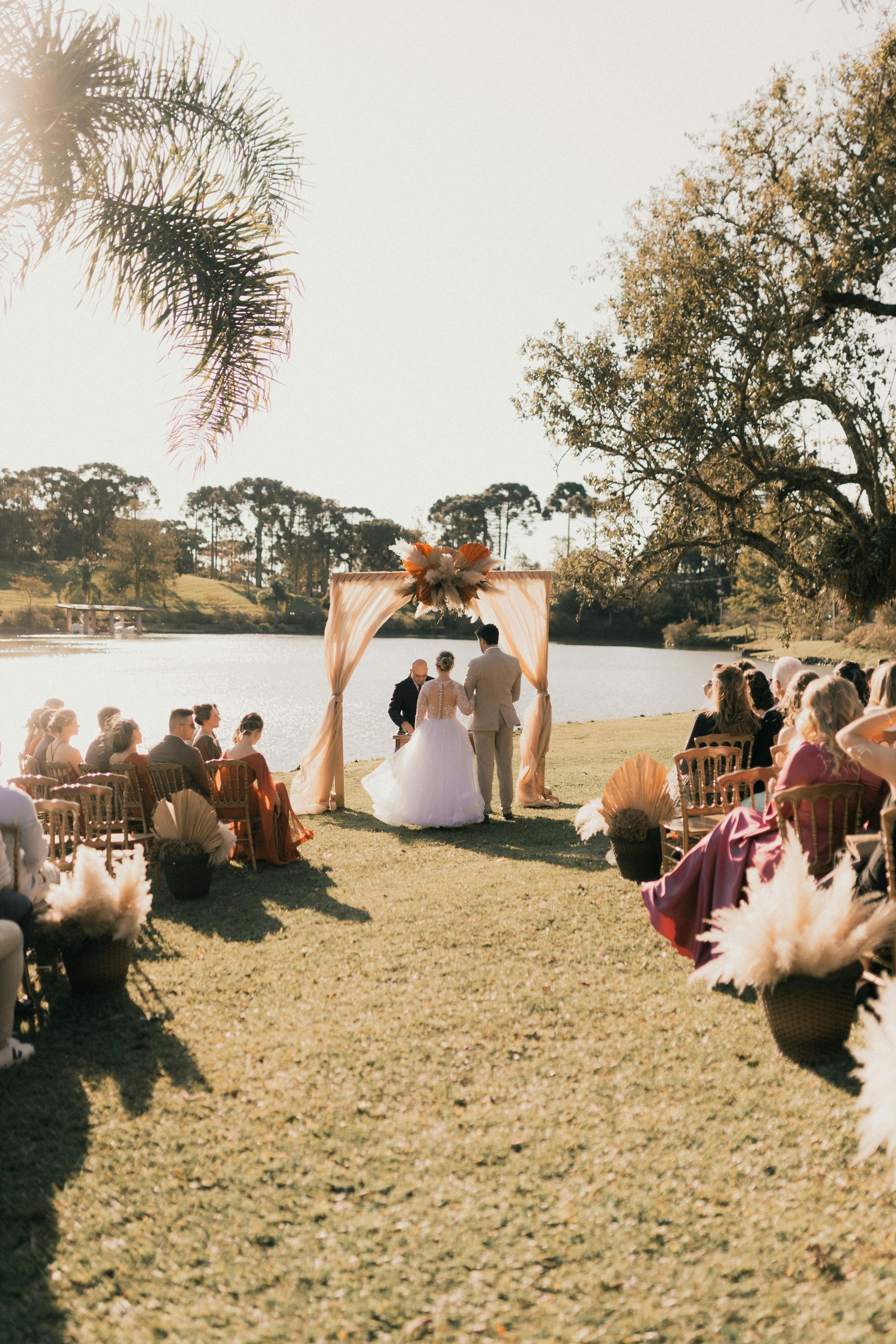 Wedding ceremony outdoors: bride and groom at altar, guests seated on grass, sunny day.