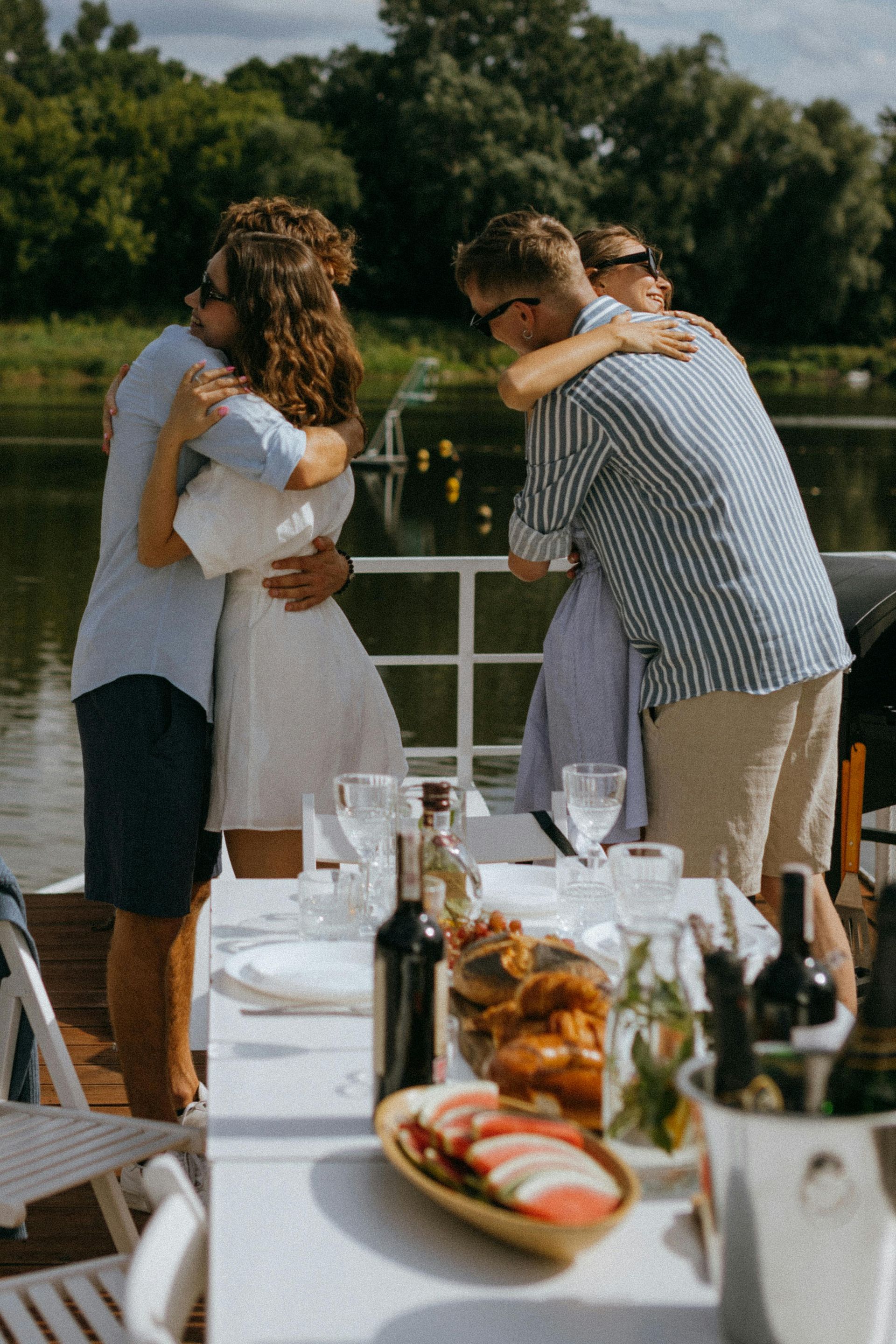 People hugging on a boat. A table with food and drinks in front of them.