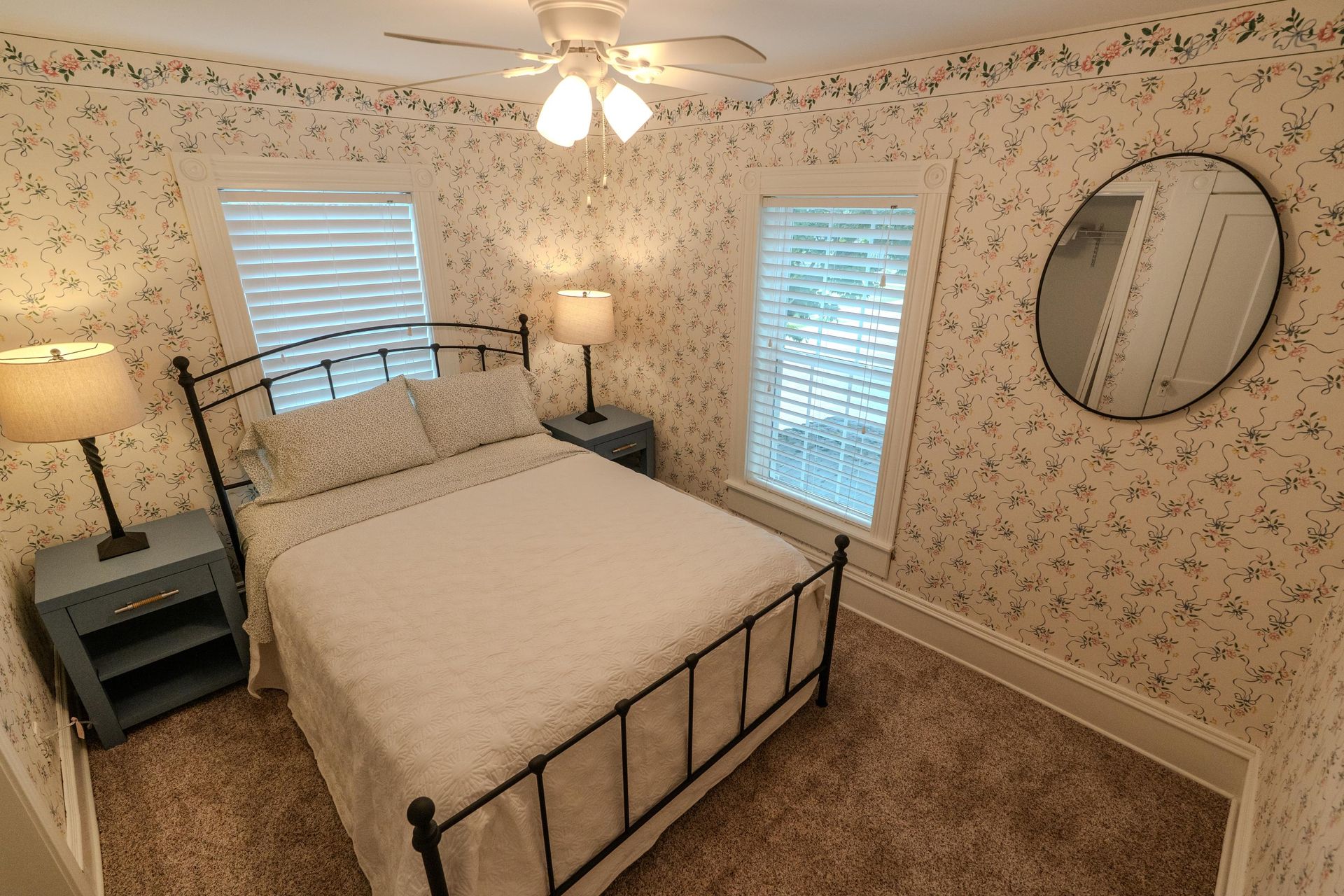Bedroom with floral wallpaper, bed with black metal frame, two nightstands, and a circular mirror.
