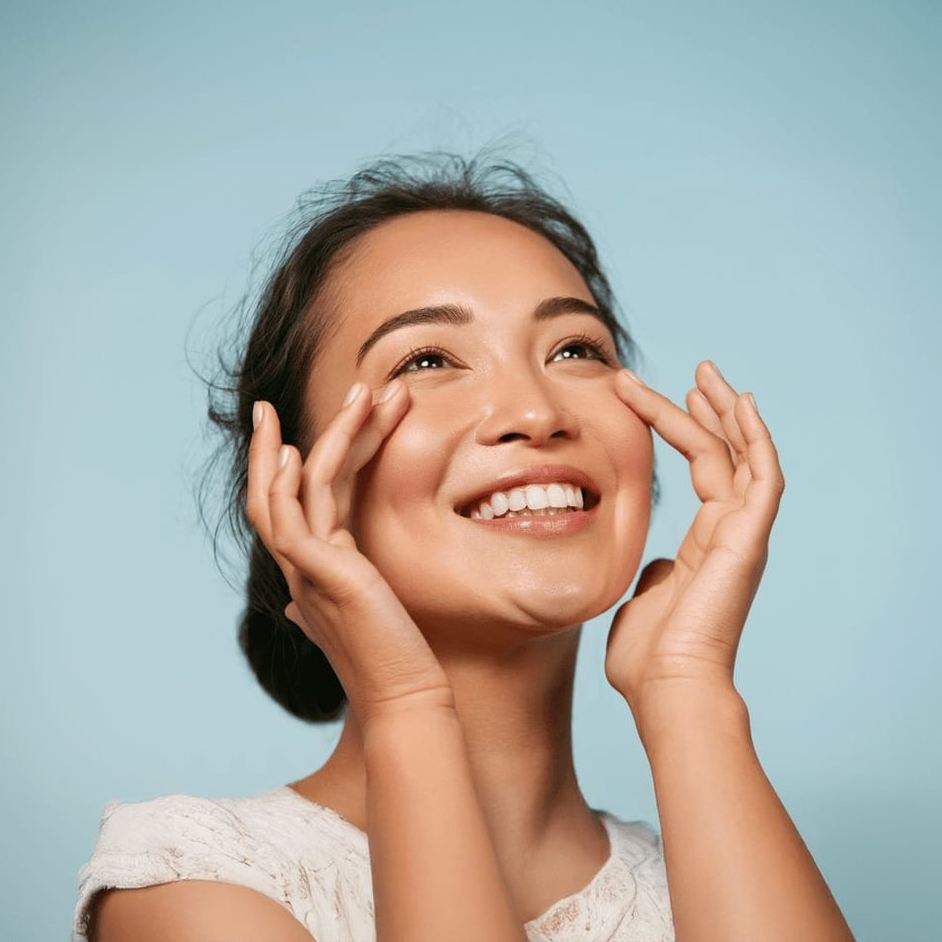 A woman is smiling and touching her face with her hands.