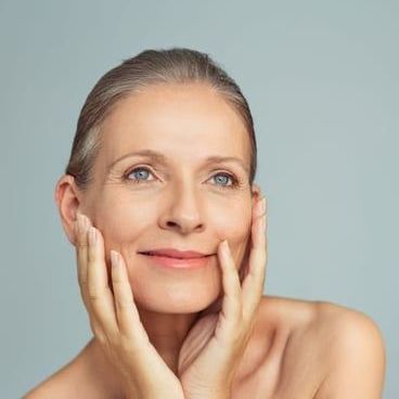 A woman is touching her face with her hands and smiling.