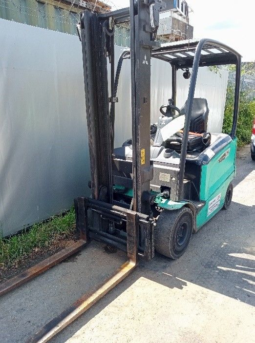 A forklift is parked in a parking lot next to a fence.