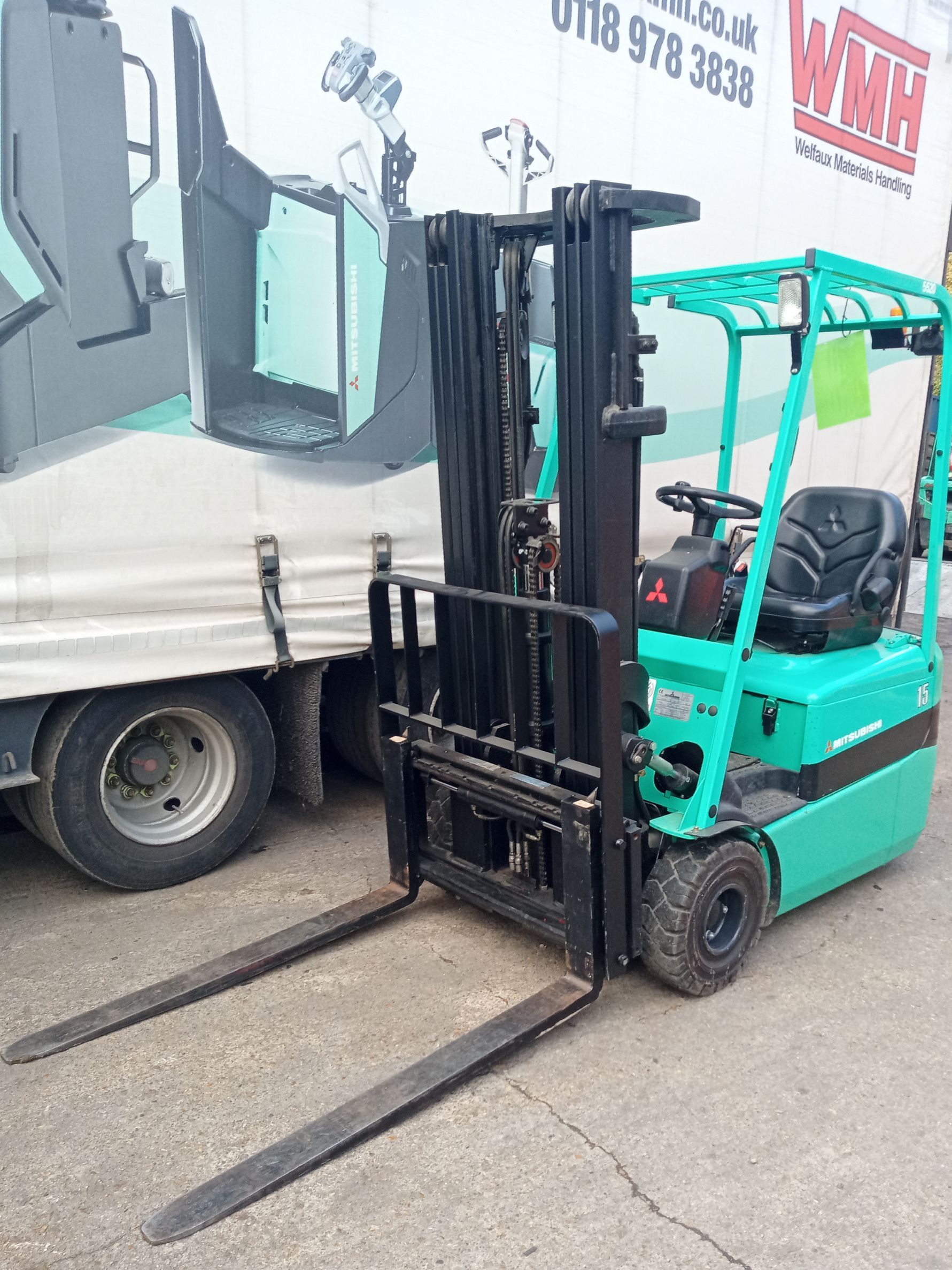 A green forklift is parked in front of a truck.