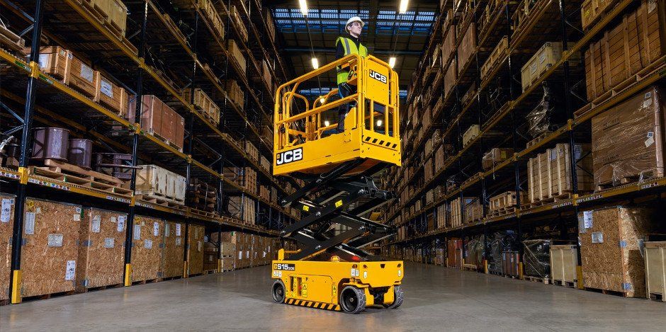 A man is riding a scissor lift in a warehouse.