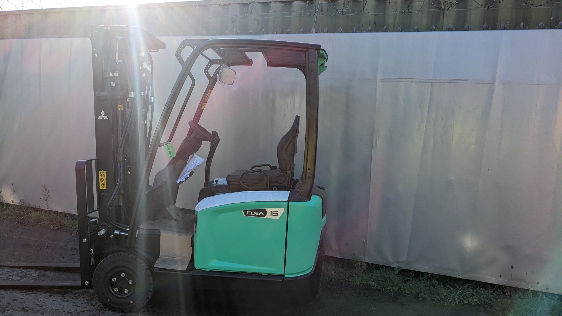 A green forklift is parked in front of a white wall. Mitsubishi