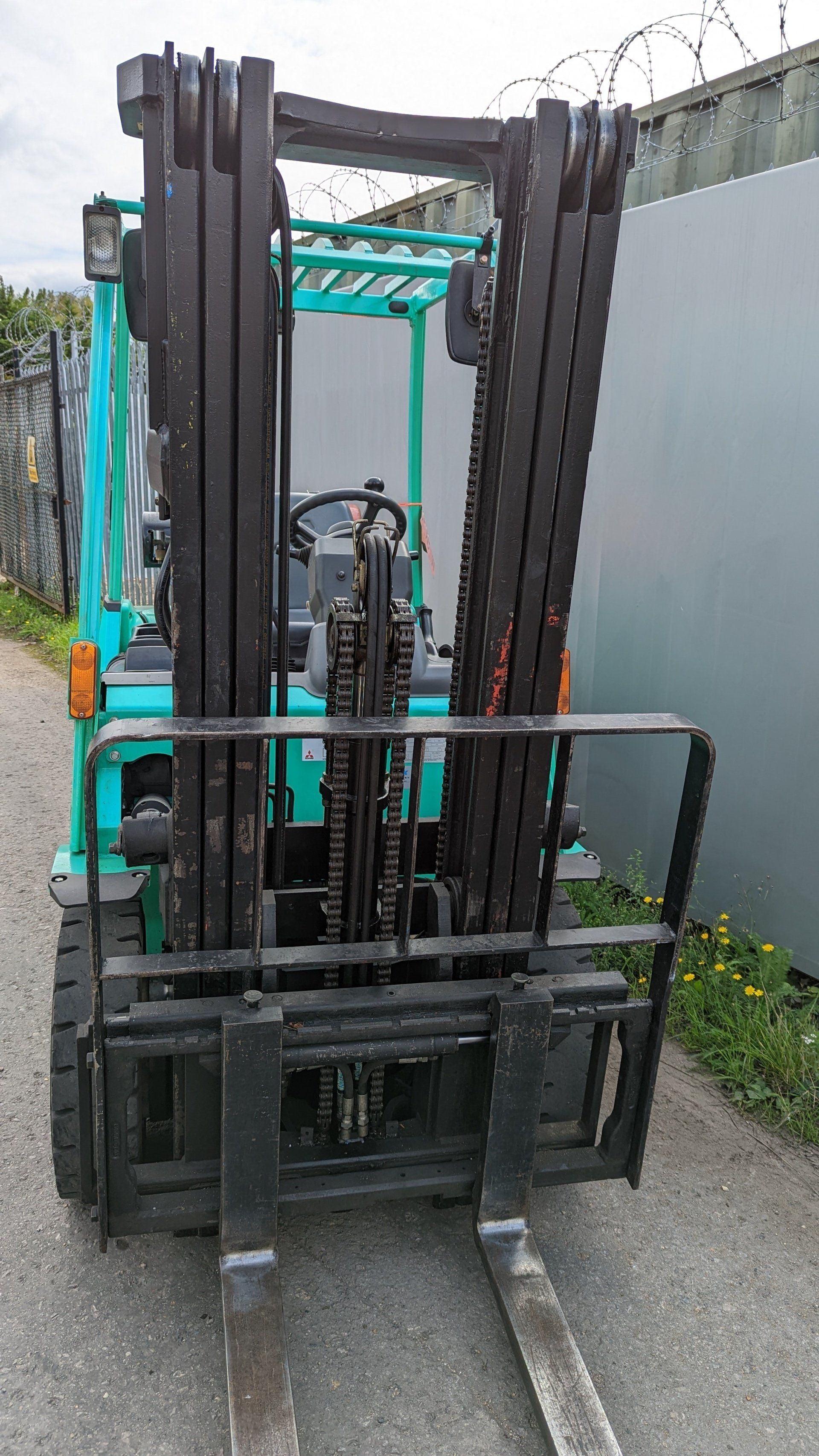 A forklift is parked on the side of the road next to a barbed wire fence.