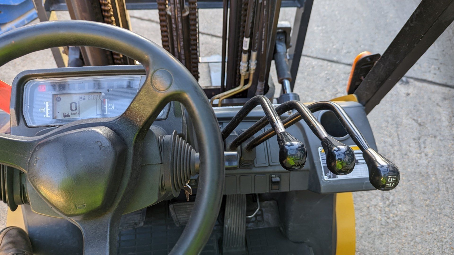 The inside of a forklift with a steering wheel and controls.