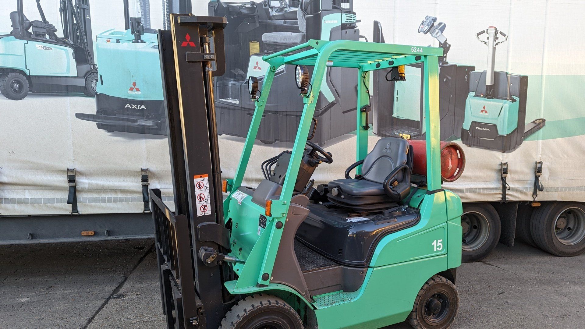 A green forklift is parked in front of a truck.