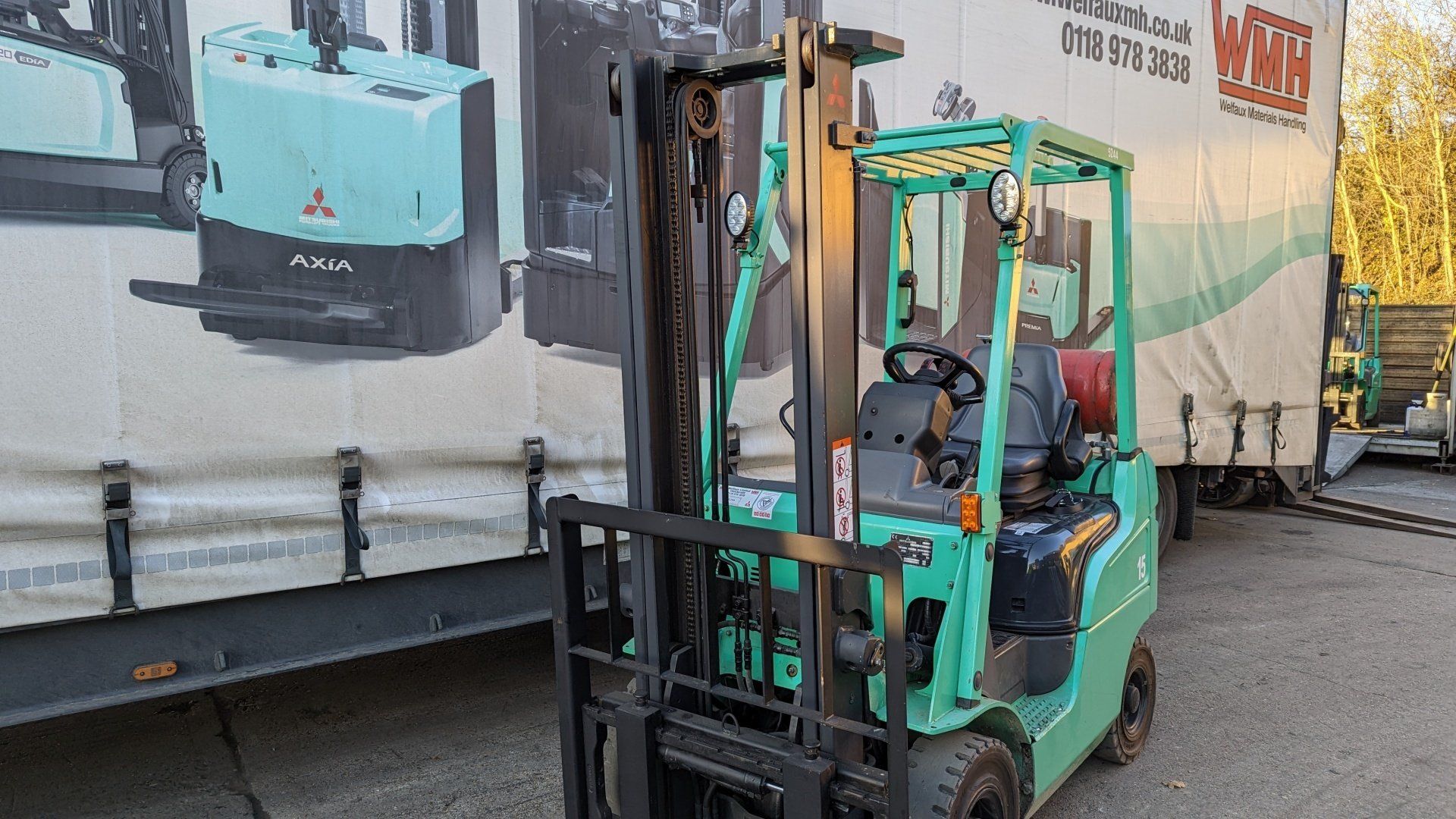 A green forklift is parked in front of a large trailer.