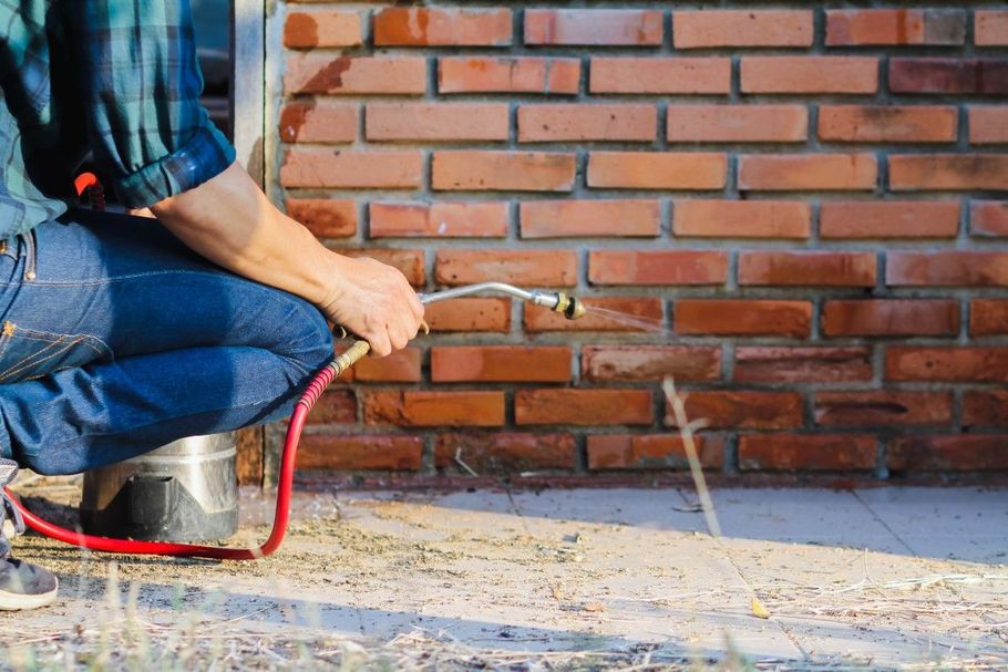Worker using a hose to spray water on a brick wall and concrete ground outdoors