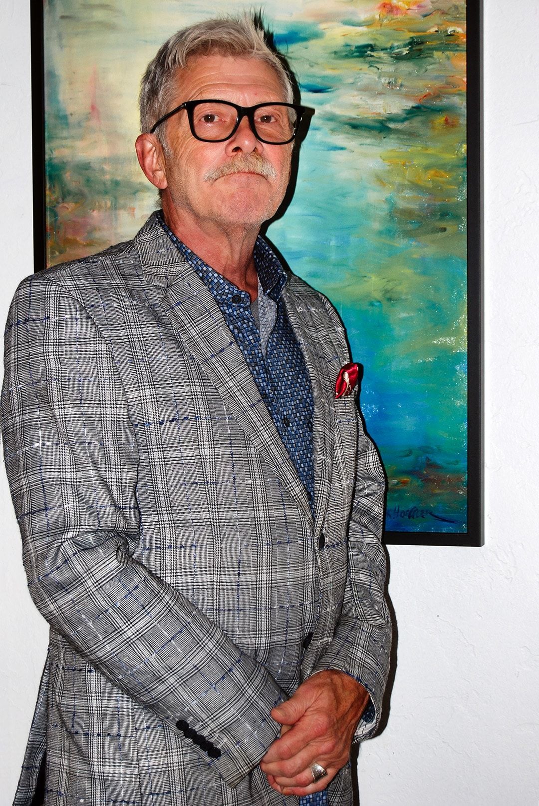 A man in a suit and glasses is standing in front of a painting.