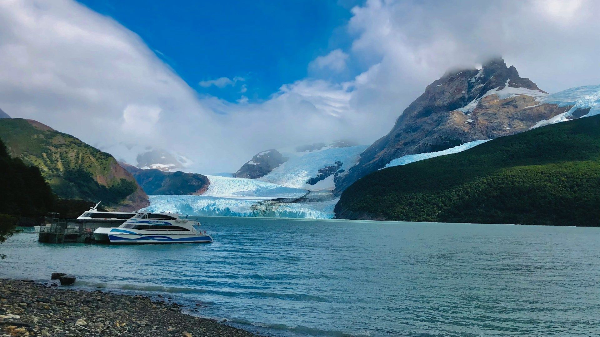 Un barco flota en un lago con montañas al fondo.