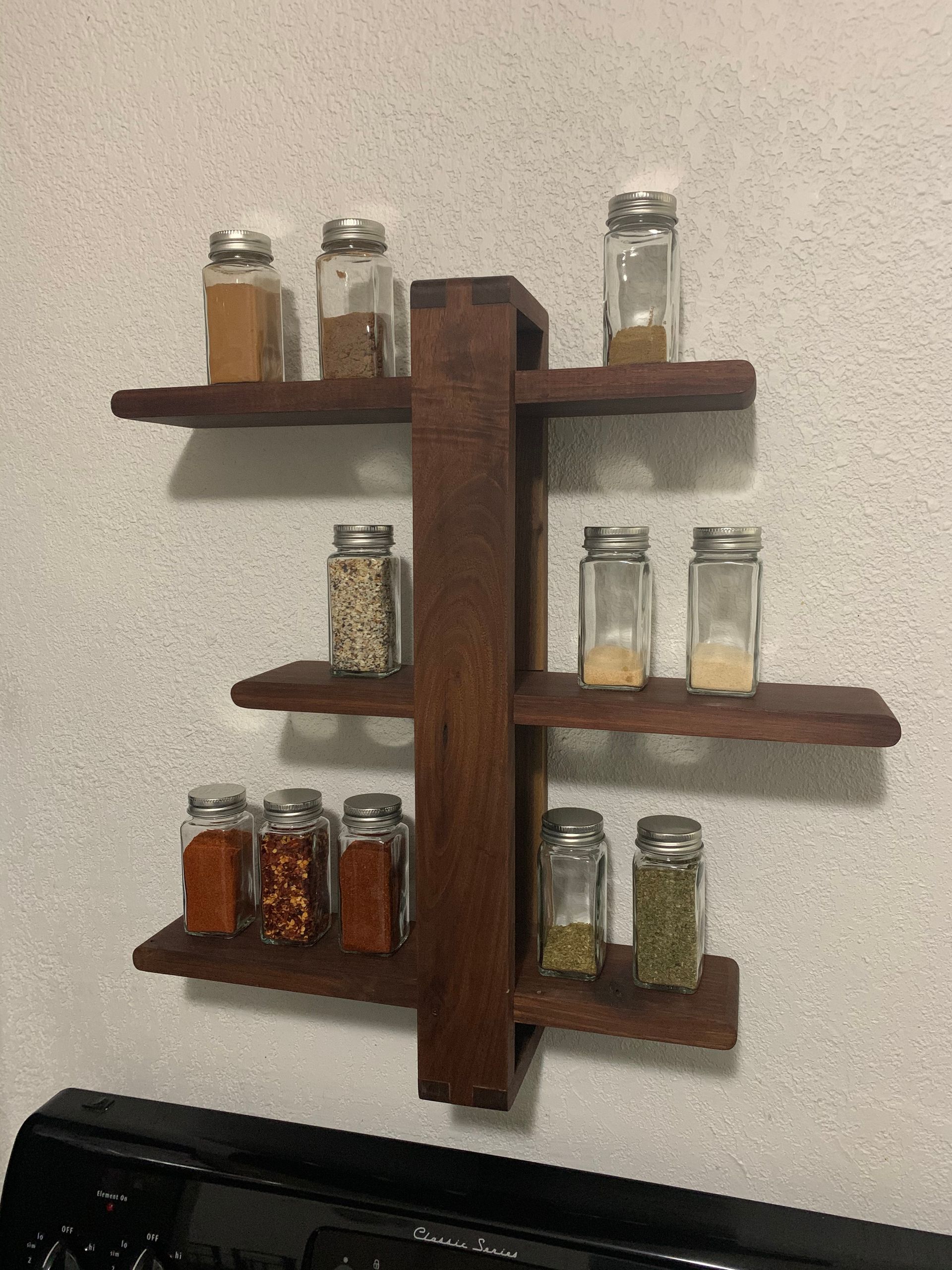 A wooden spice rack is hanging on a wall next to a stove.