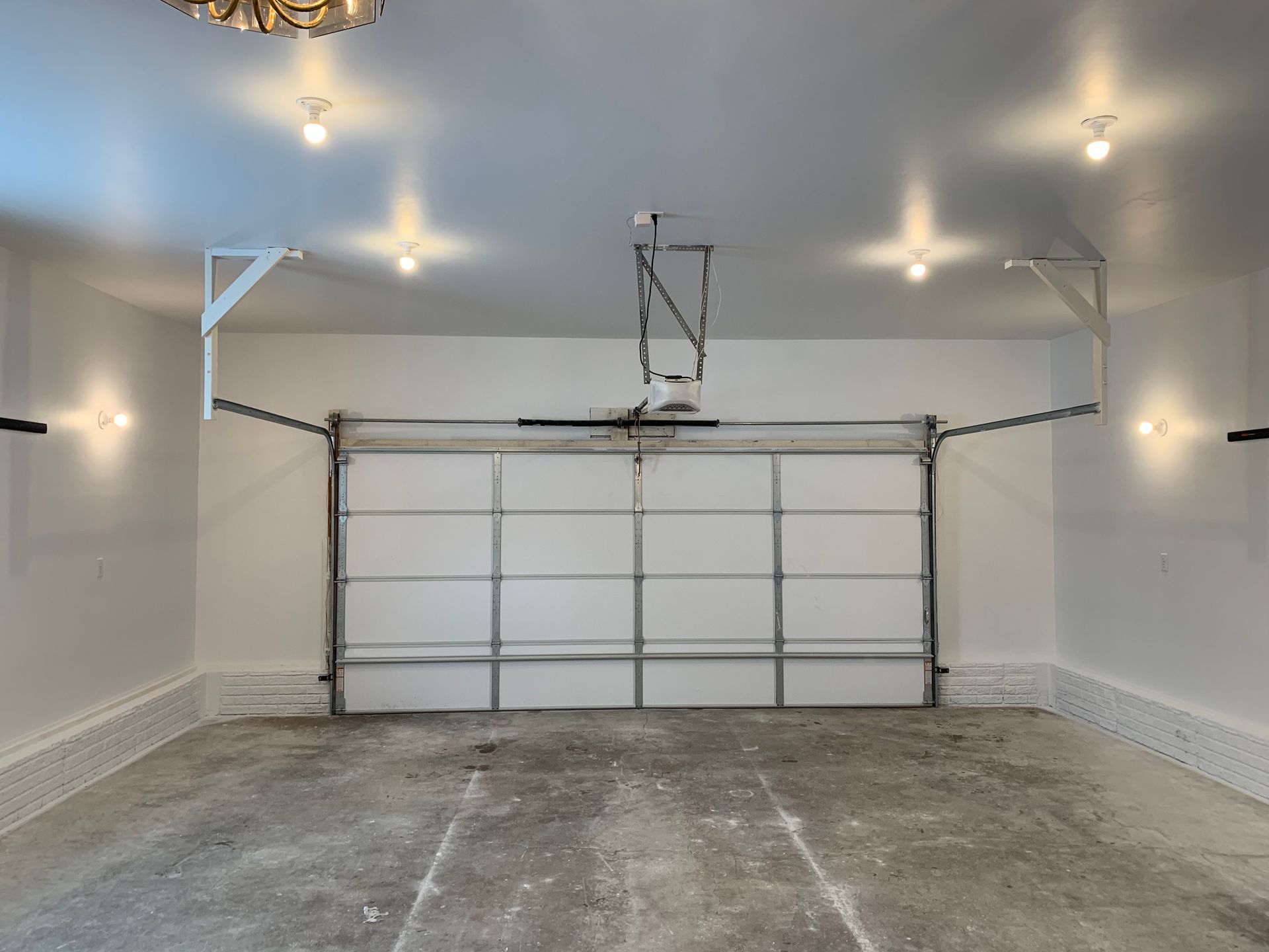 An empty garage with a garage door open and a chandelier hanging from the ceiling.