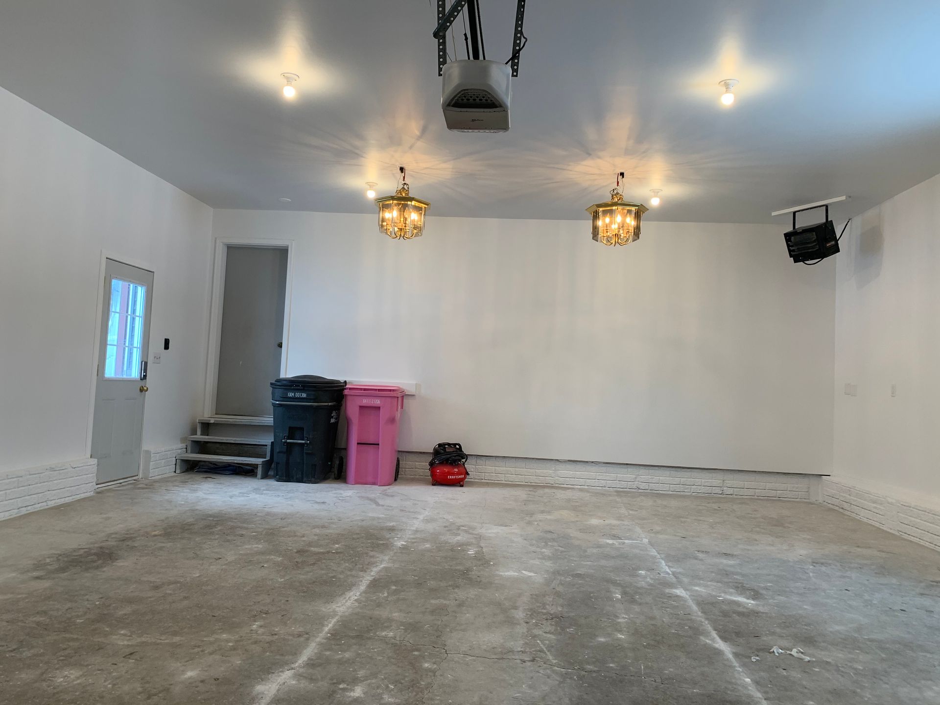 An empty garage with white walls and a pink trash can.
