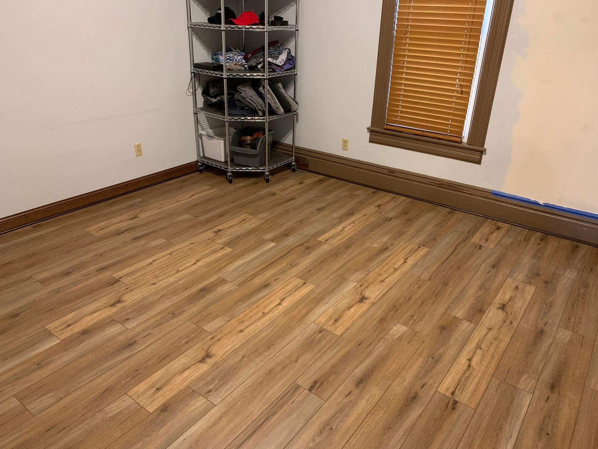A room with a wooden floor , a shelf , and a window.