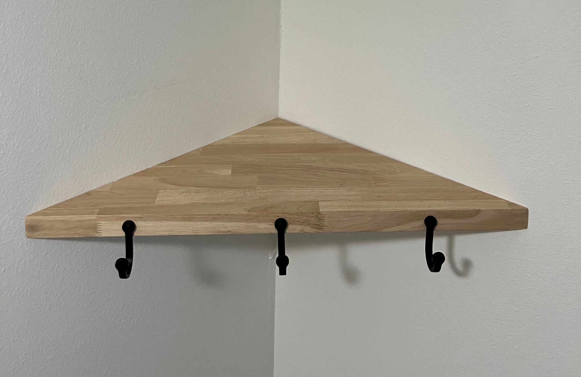 A wooden corner shelf with hooks attached to it