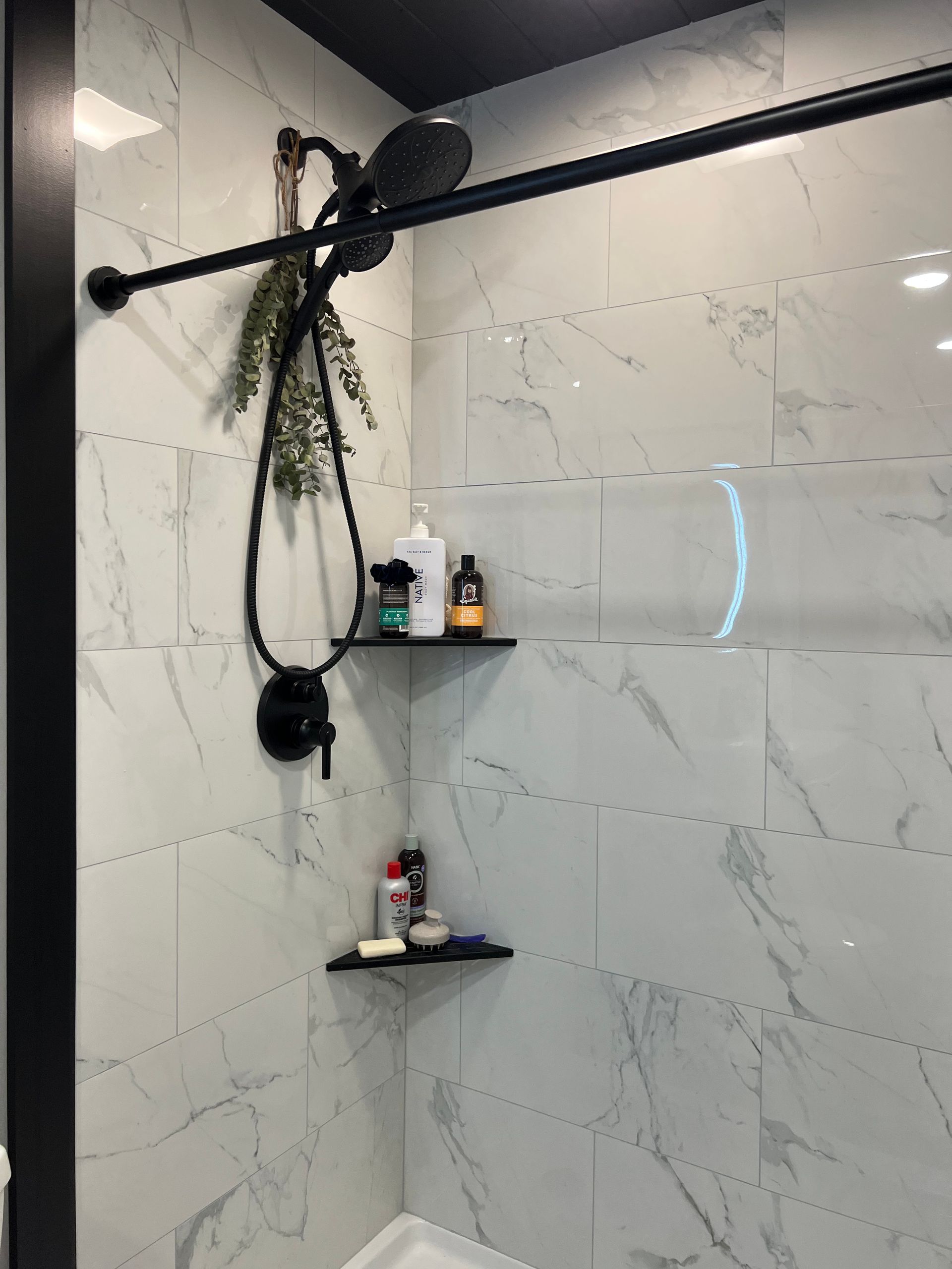 A bathroom with a shower head hanging from the ceiling and a shelf.