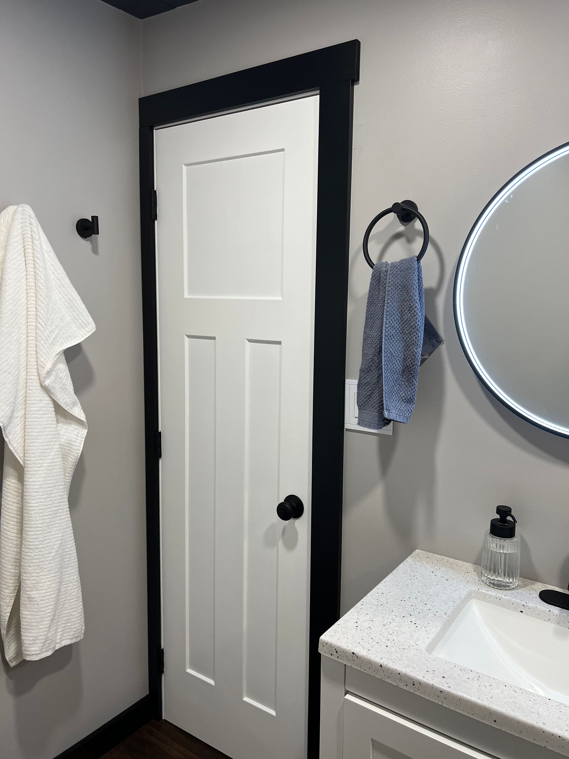 A bathroom with a white door , sink , mirror and robe hanging on the wall.