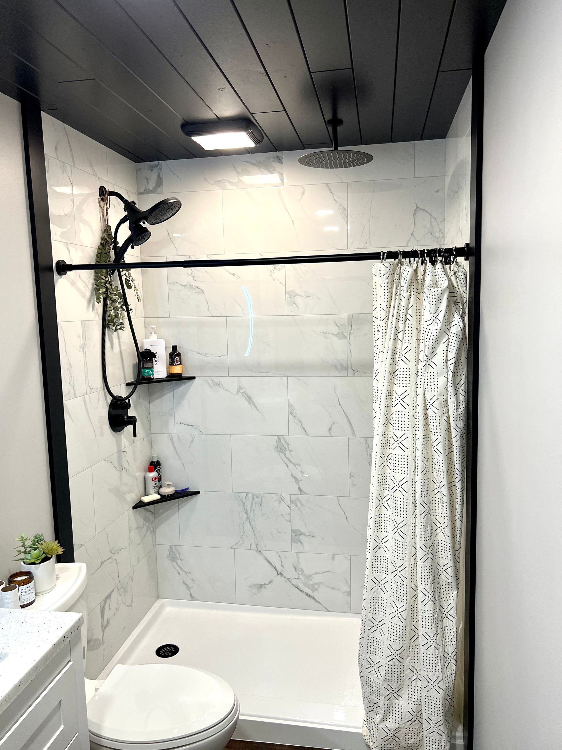 A bathroom with a shower , toilet , sink and black ceiling.