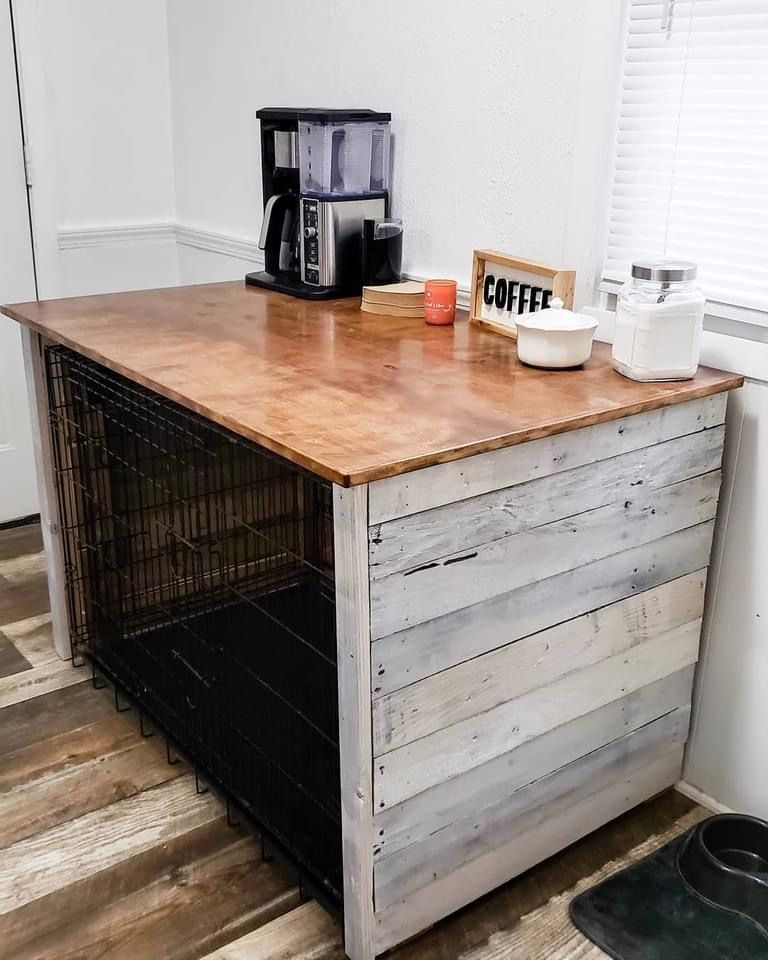 A dog crate is sitting under a wooden table in a kitchen.