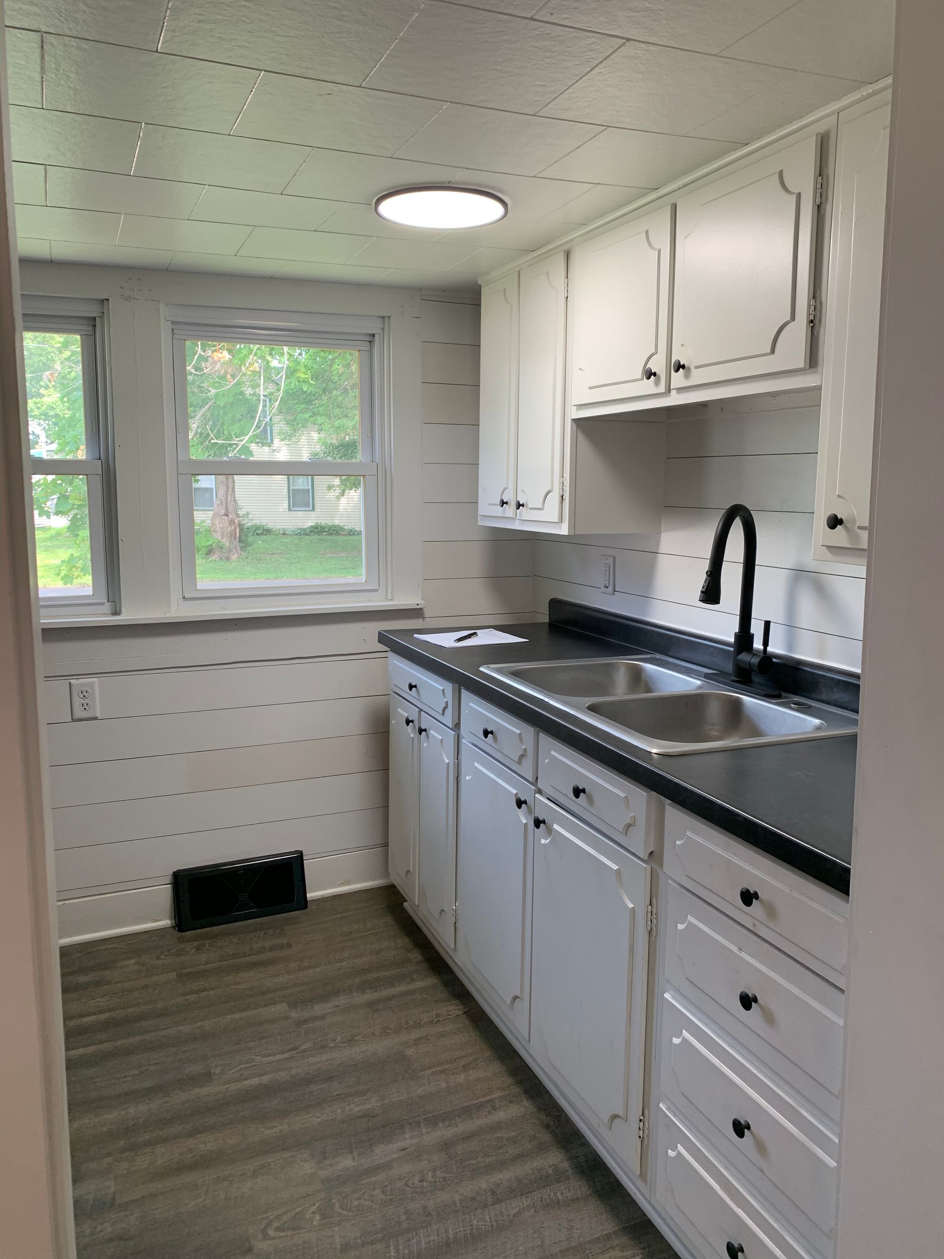A kitchen with white cabinets , a sink , and a window.