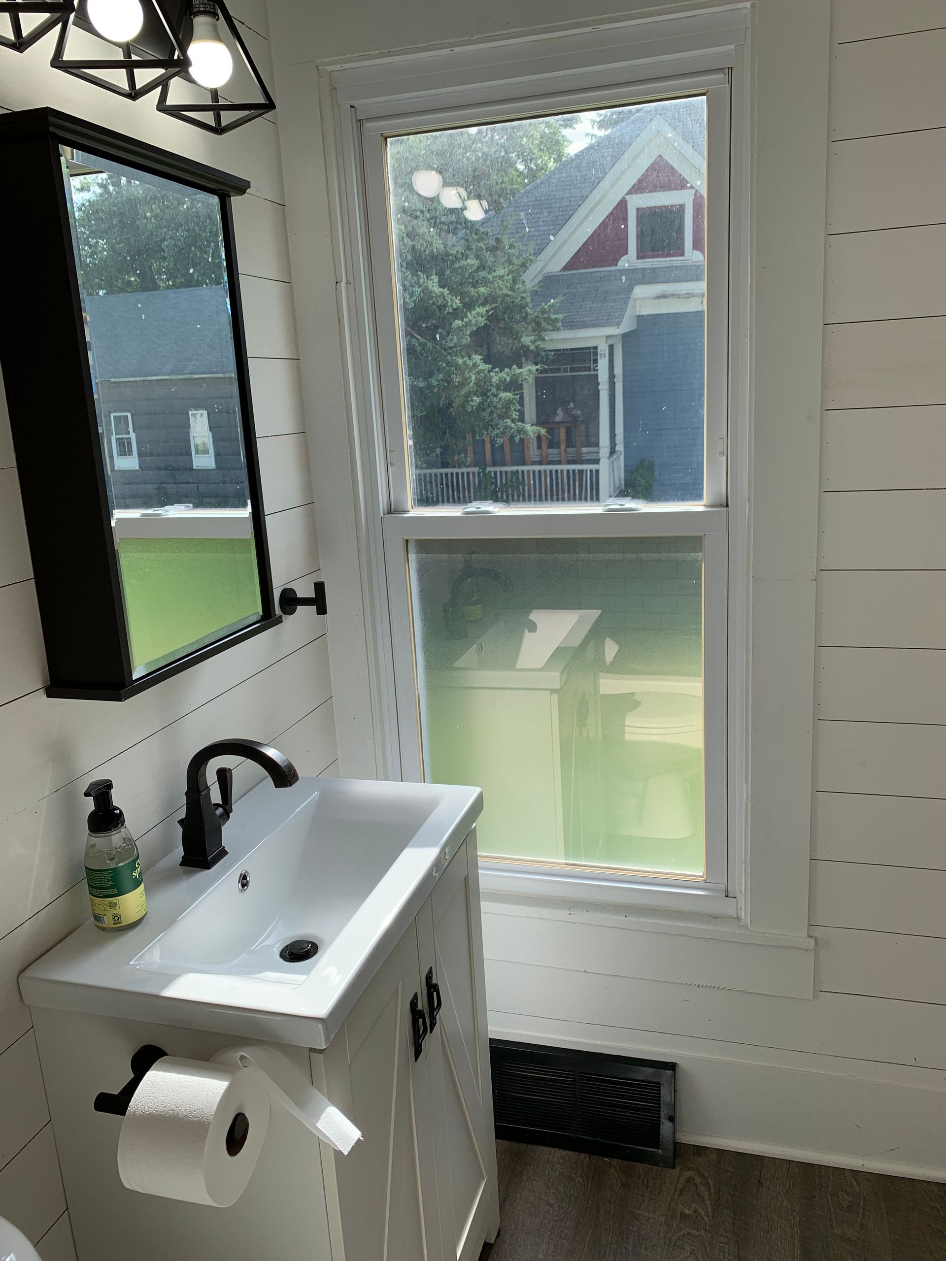 A bathroom with a sink , mirror and window.