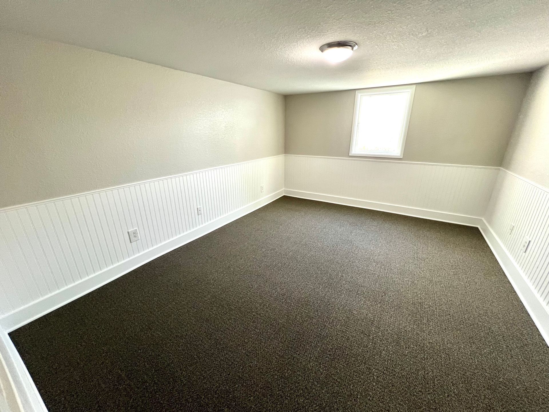 An empty room with a carpeted floor and a window.
