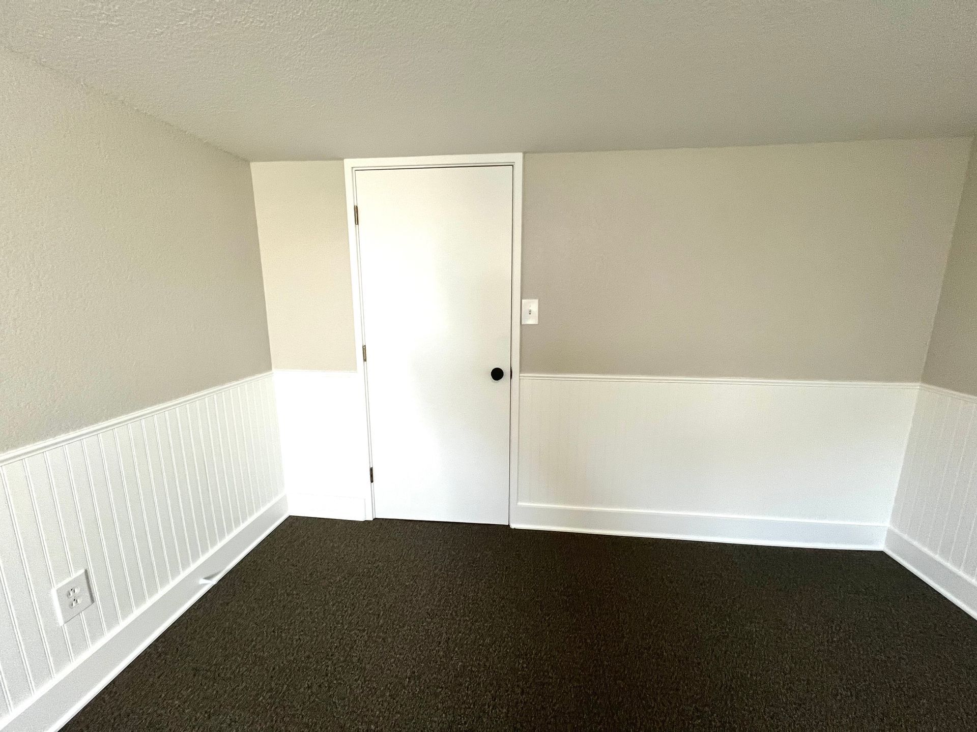 An empty room with a door and a carpeted floor.