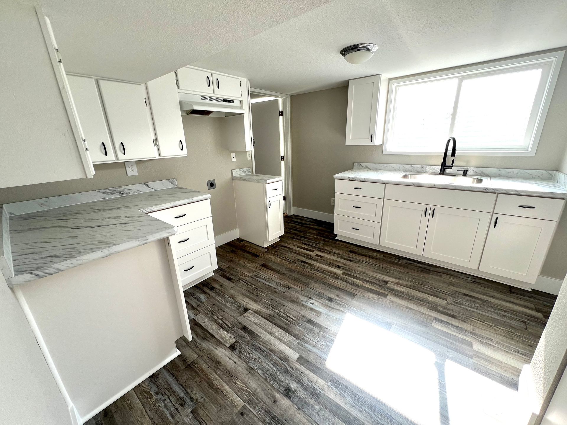 A kitchen with white cabinets , a sink , and a window.